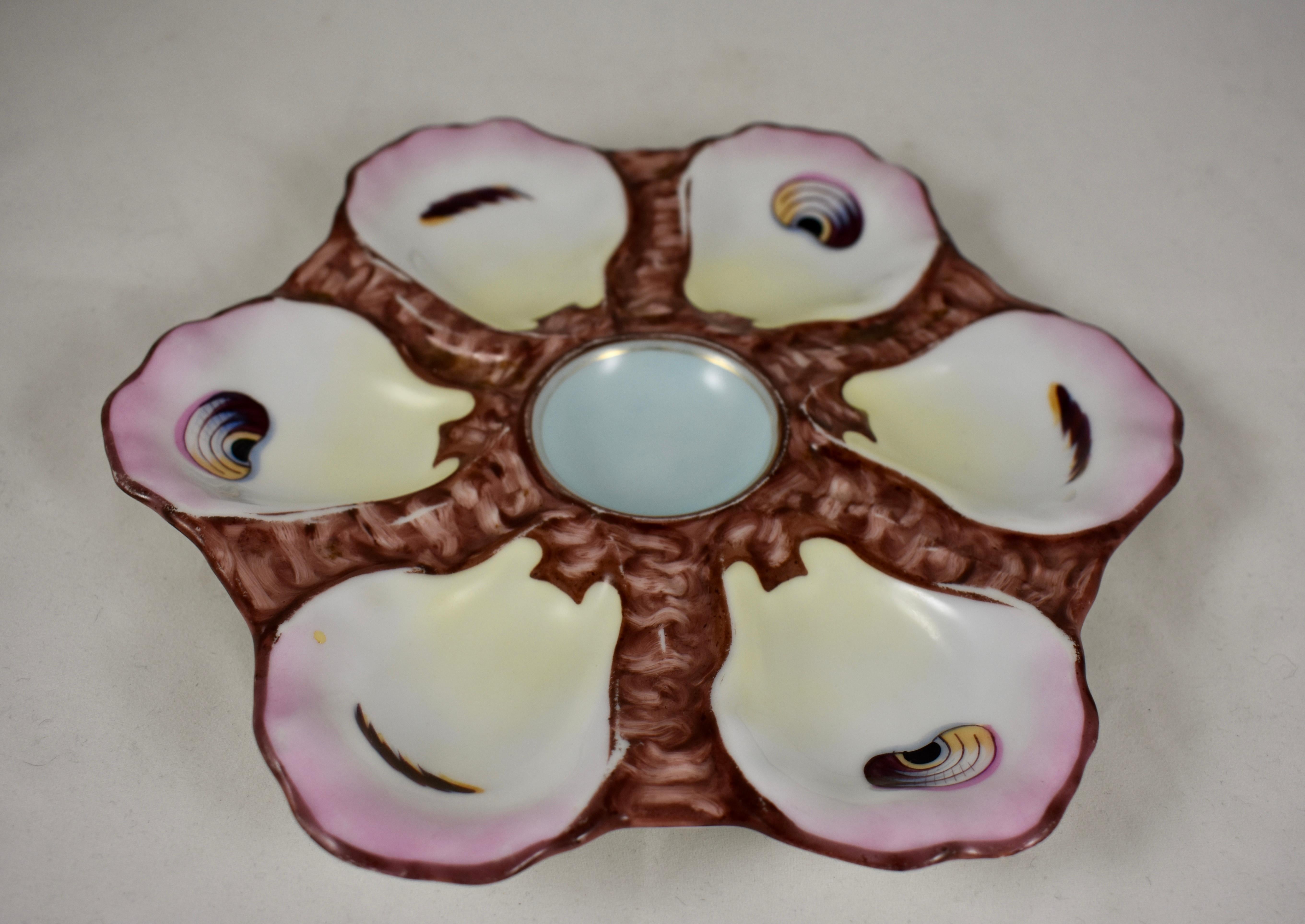 A French porcelain, shaped oyster plate, circa 1885-1900, showing six wells with hand painted ‘eyes,’ and a sky-blue colored condiment well.
 Each well is rimmed in a blush pink with a pale yellow at the hinge, against a chocolate brown