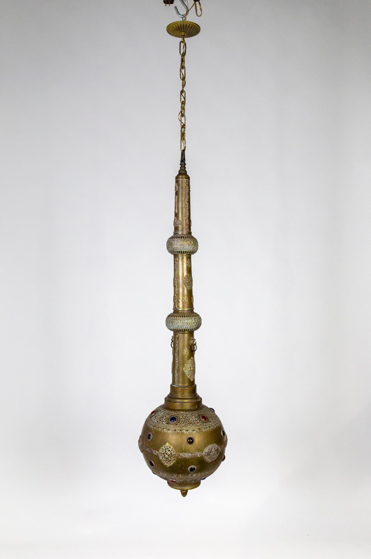 This long, narrow, hanging lamp is in the form of a narrow cylinder ending with a large ball. It mimics an Indian rose water sprinkler or Gulab Pash. Handmade of brass, with intricate, punched-out shapes and depiction of the Taj Mahal, by which