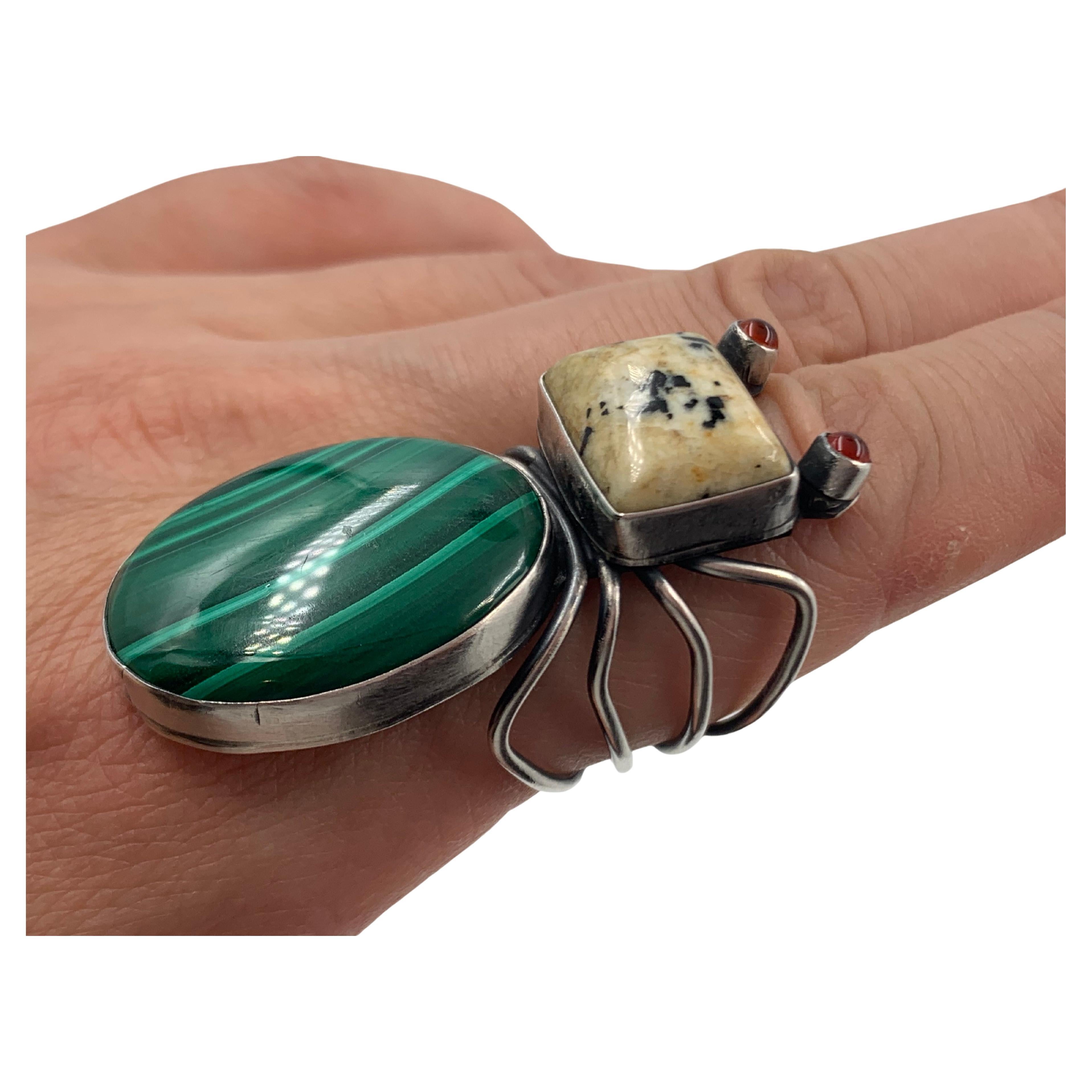 Spinnenring aus Sterlingsilber vom Navajo-Silberschmied Herbert Ration. Die Spinne besteht aus Edelsteinen: einem Körper aus Malachit, einem Kopf aus Jaspis und Augen aus Karneol. Bei einigen südwestlichen Stämmen stehen Spinnen für Kreativität,