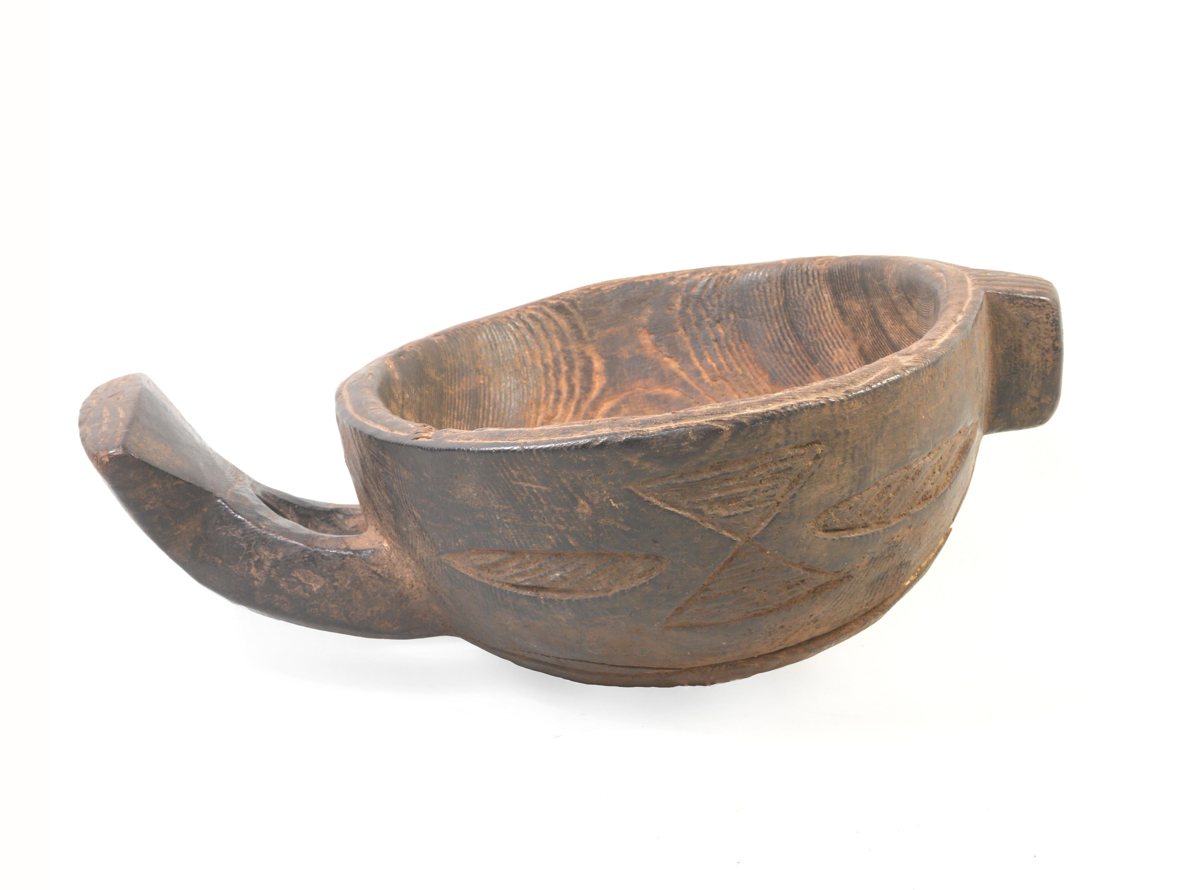 This well used, mid-twentieth century wooden bowl is a skeuomorph from the Grassfields region of Cameroon. Its form, with a pour spout at one end and an ergonomic handle at the other, is derived from traditional terracotta bowls used in the