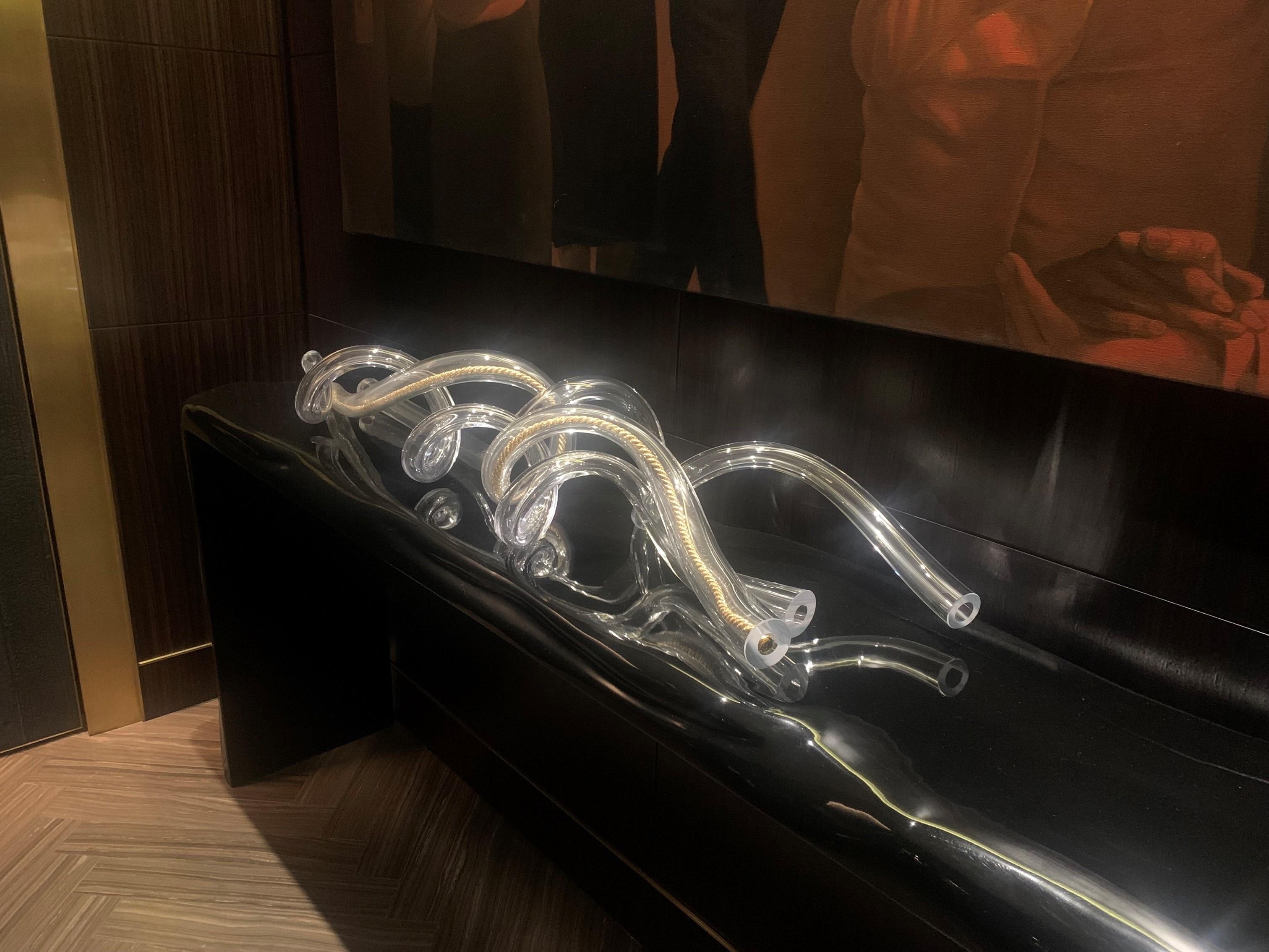 Offered is a long, coiled, transparent blown-glass sculpture that rests on a long console or as a table centerpiece and did not come with a stand. 

The sculpture is comprised of organically twisted tubes of handblown glass with cut and polished