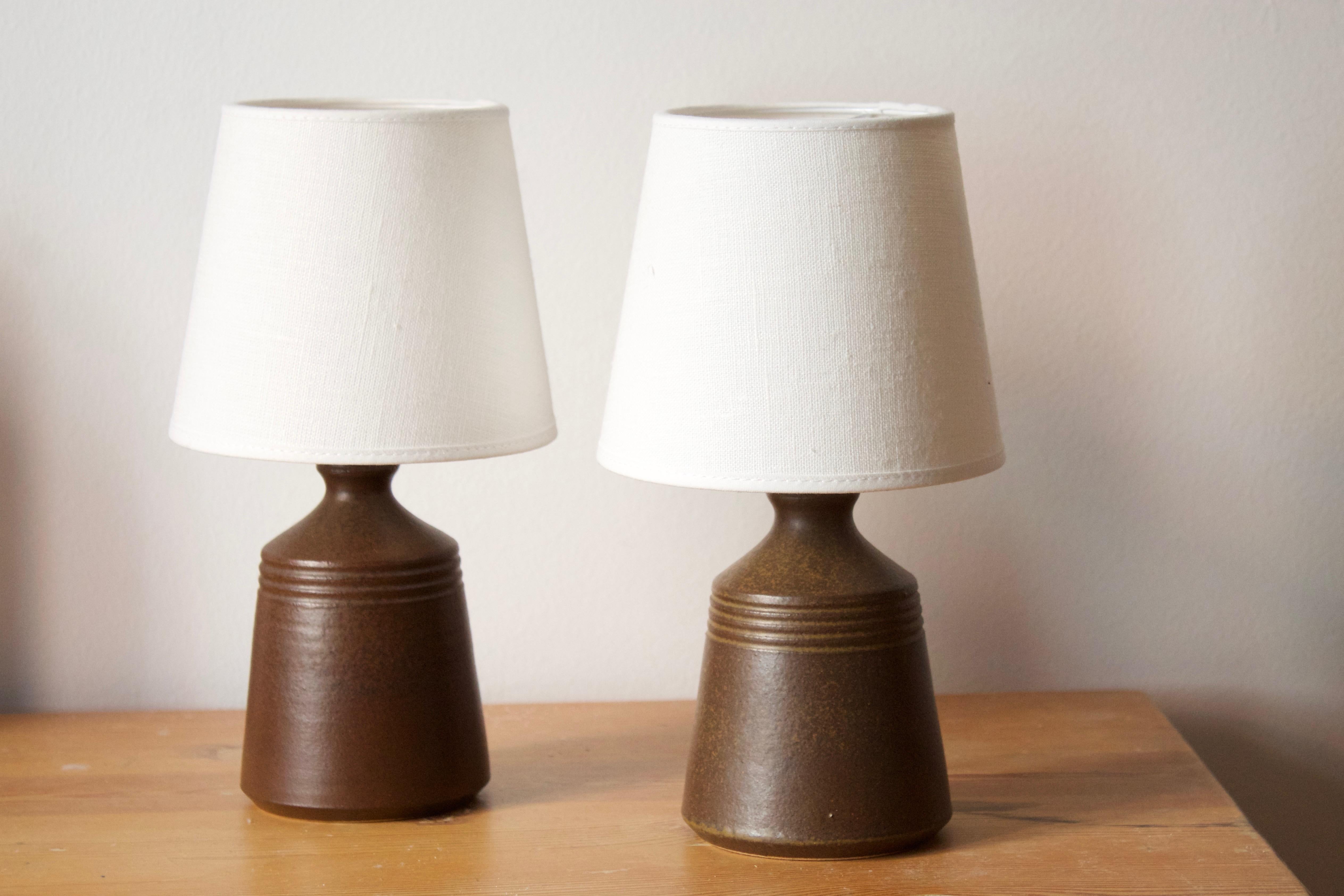 A pair of small table lamps. Designed and produced by Skottorp Stengods. Signed and stamped. Features simple incised decoration. 

Stated dimensions exclude lampshade. Height includes socket. Sold without lampshades.

Glaze features a brown color.