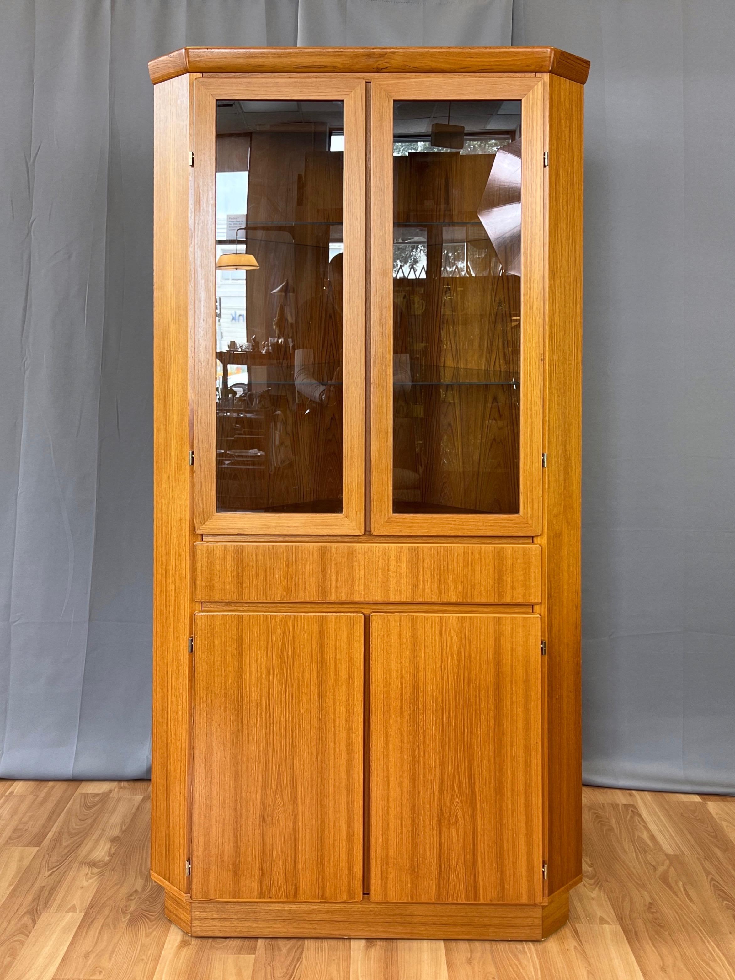 A 1970s Danish modern Skovby Møbelfabrik tall teak lighted corner display cabinet with glass doors and shelves.

Clean lines and handsomely figured teak from top to bottom. Upper half with a pair of glass doors, behind which are two