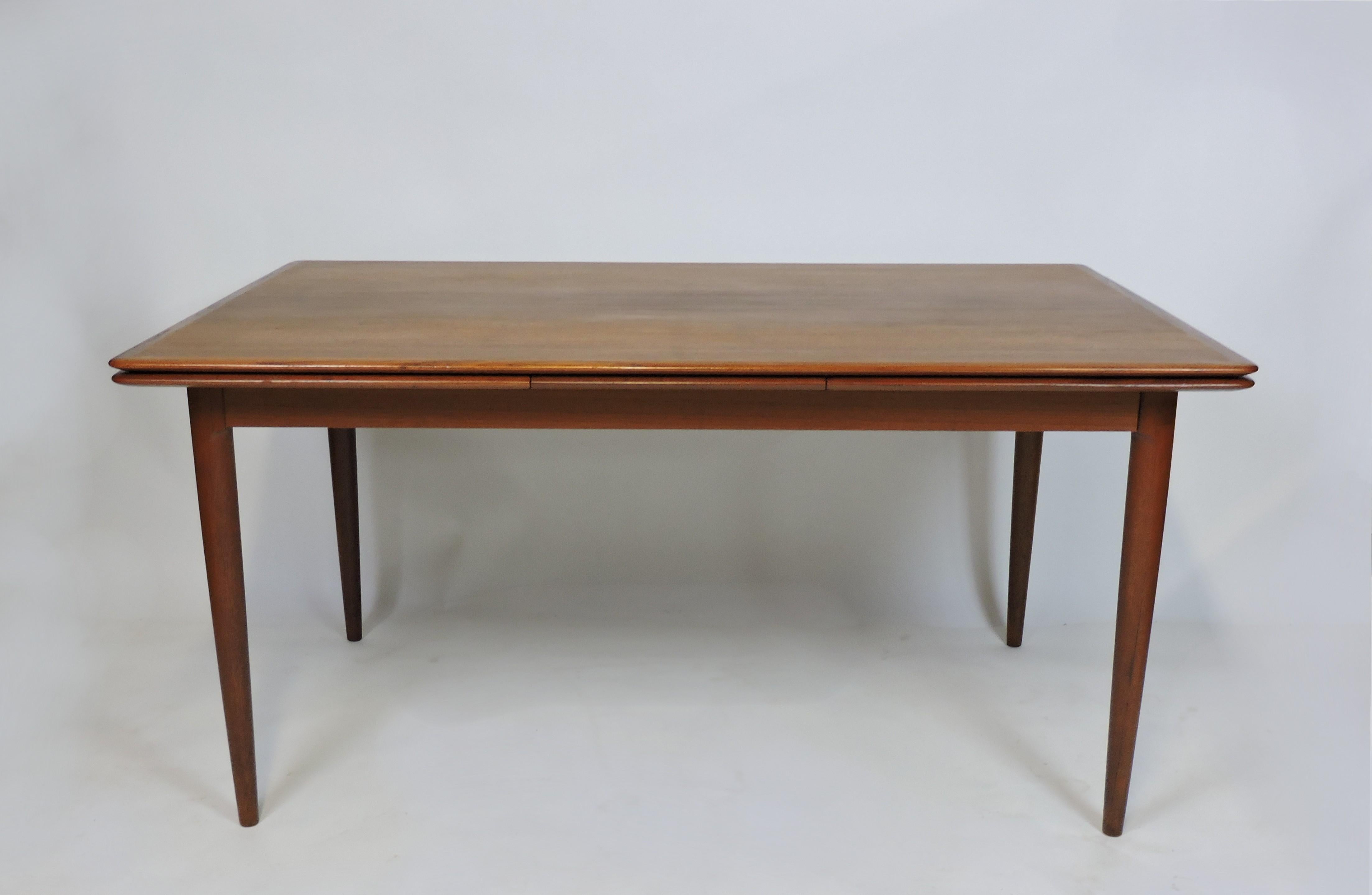 Beautiful and large teak dining table manufactured by Skovmand & Andersen in Denmark and imported to the US by Moreddi. This table has an elegant design with graceful solid teak tapered legs and two self-storing leaves that slide out to extend the