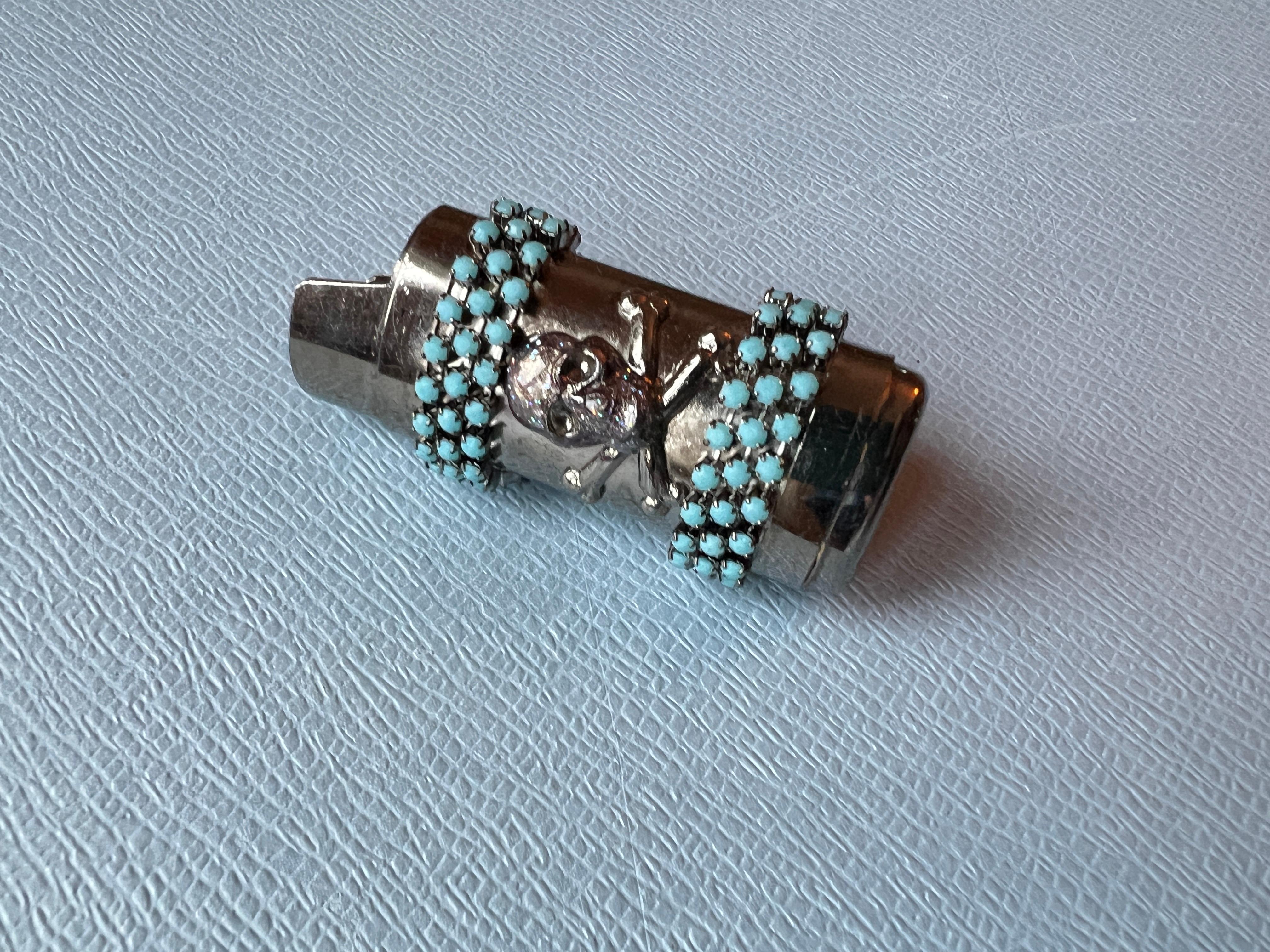 Skull and Bone Light Holder with turquoise Rhinestone Crystals, Ruthenium Plated in Paris, Vintage 2008. 

Measurement: Height 2 inches,
Width 0.95 inches

Condition: Has lost a bit of shine and features minor markings indicative of its age and