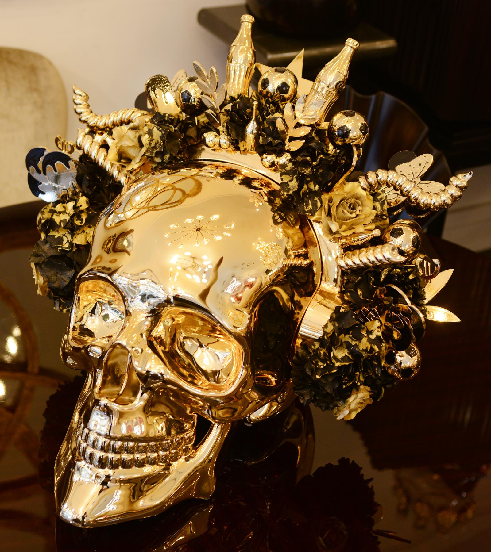Sculpture skull golden youth. Skull made in marble
dust resin and chromed in gold finish. With head piece
decorated with different golden youth symbols. Champagne
bottle, Minnie Mouse, ice cream, flowers with gold leaf, Euros,
soccer