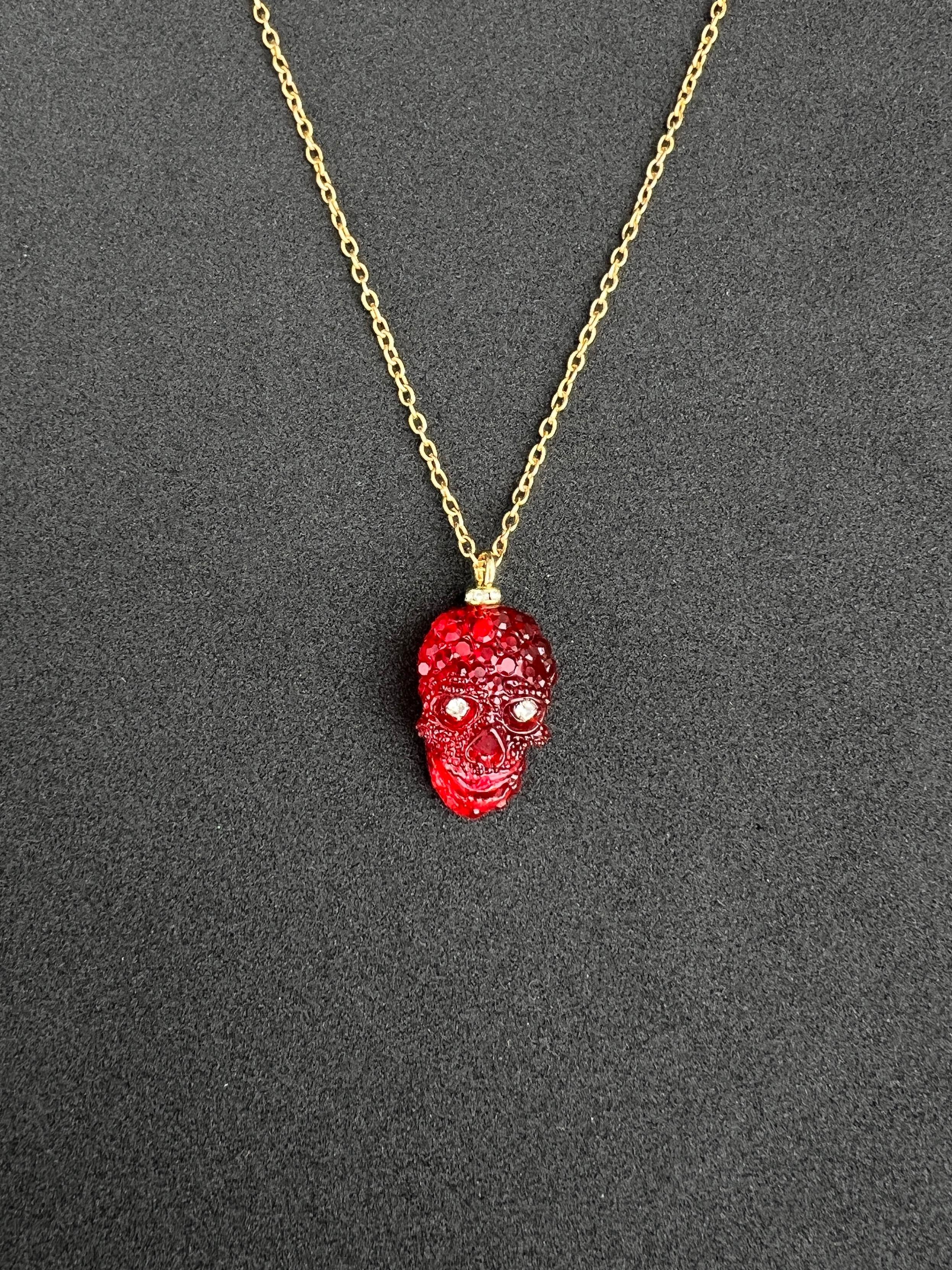 Questa splendida collana con ciondolo è dotata di una catena d'oro che non si appanna e che garantisce una lucentezza e una durata durature. Sospeso alla catena c'è un vibrante teschio in resina rossa, intricato e impreziosito da scintillanti occhi