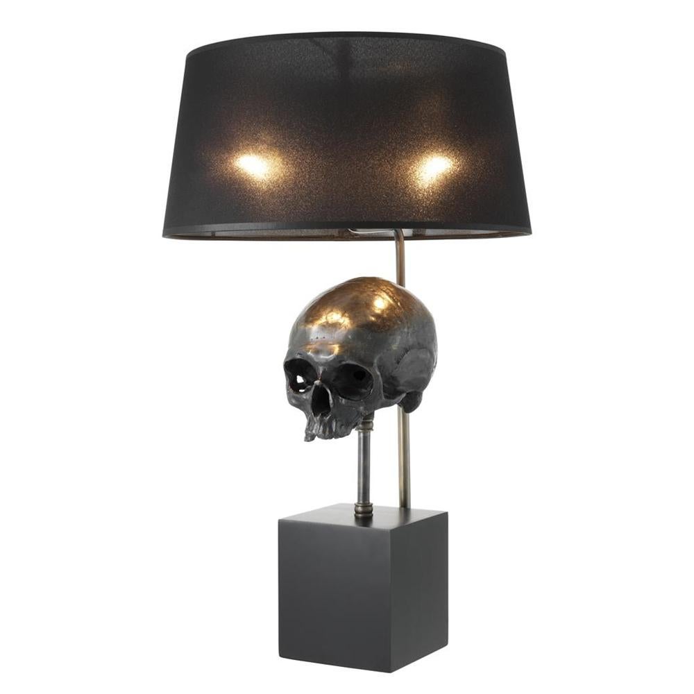 Table lamp skull with solid brass skull in aged brass
finish, on iron base in black finish. Lamp with a black 
transparent shade.
 
