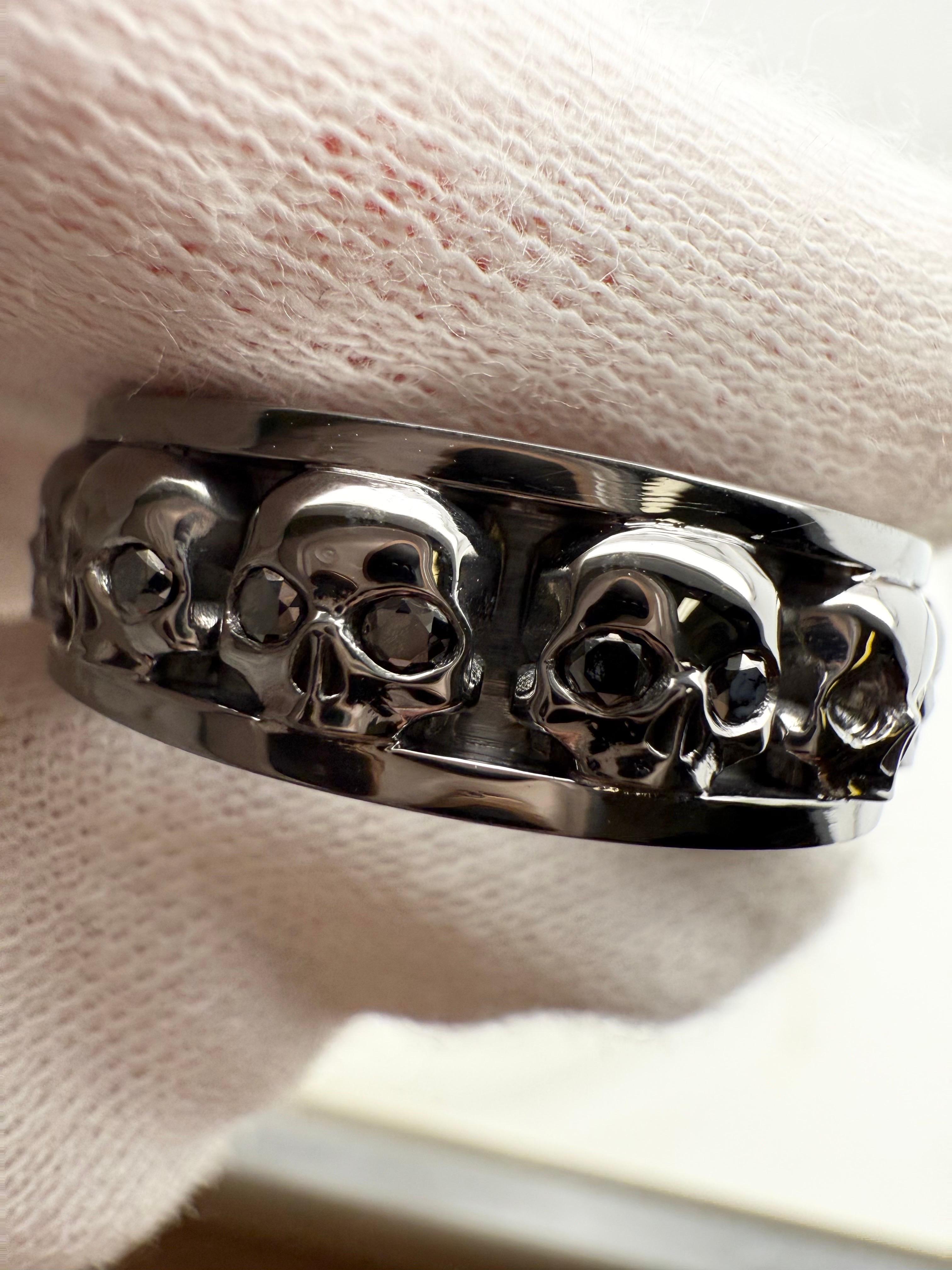 Único en su especie, nuestro emblemático anillo Miami Jewels hecho con 12 calaveras, oro negro y diamantes negros de gran calidad. Tiene 7 mm de ancho y está hecho a la perfección, elaborando cada calavera por separado y uniéndolas para crear una