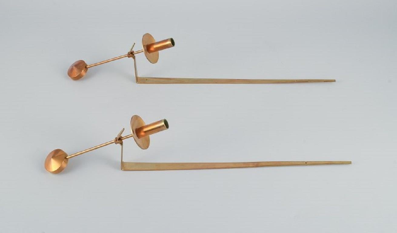 Skultuna, Sweden, a pair of brass candlesticks for wall hanging.
Designed by Pierre Forsell. 
Marked. 
In excellent condition. 
Total length 48.5 cm.