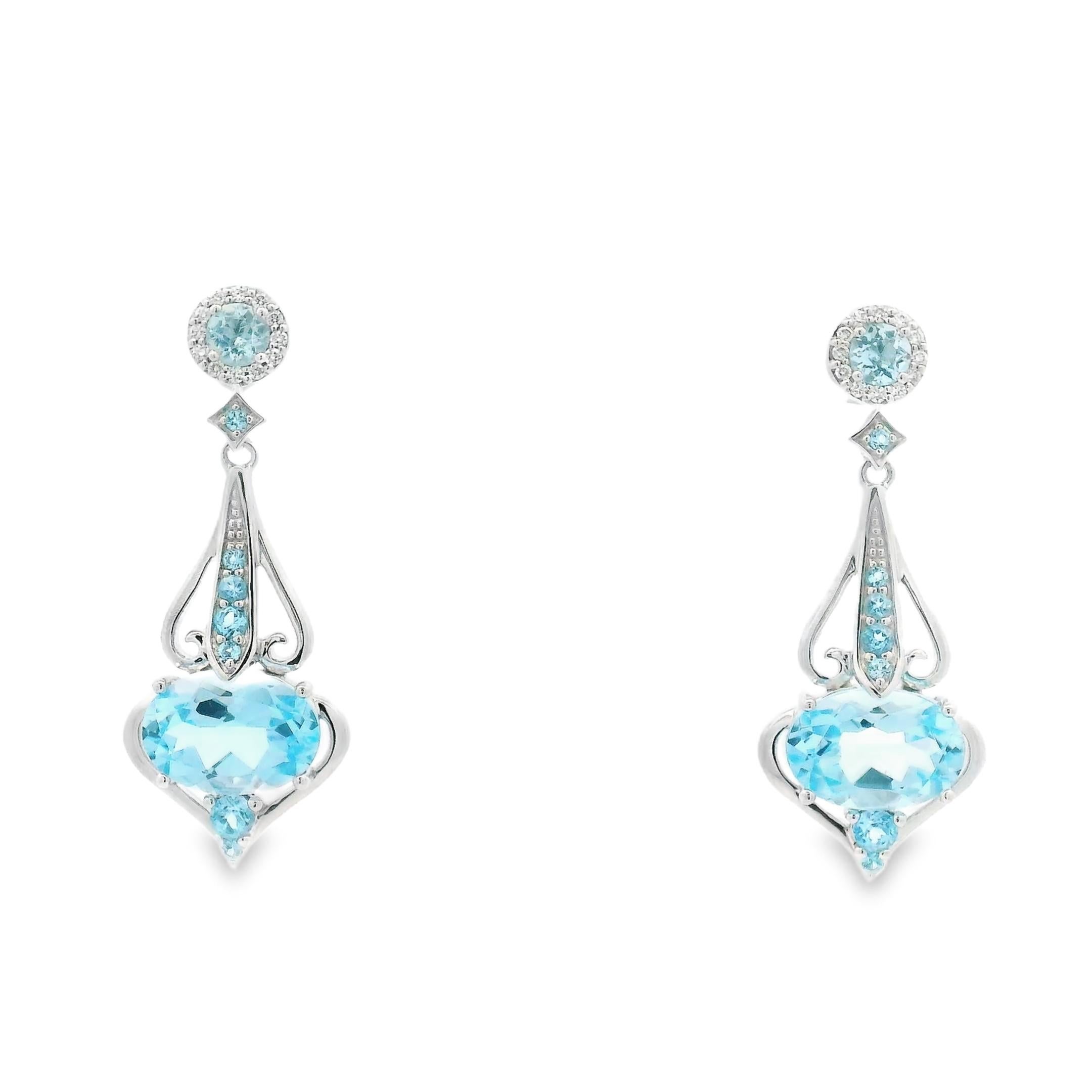 These sky blue topaz drop earrings in 14K white gold blend graceful curves with bright, airy color. Each earring features a faceted oval-cut topaz at the base, cradled in a sculptural open setting that mimics the shape of a heart. A line of