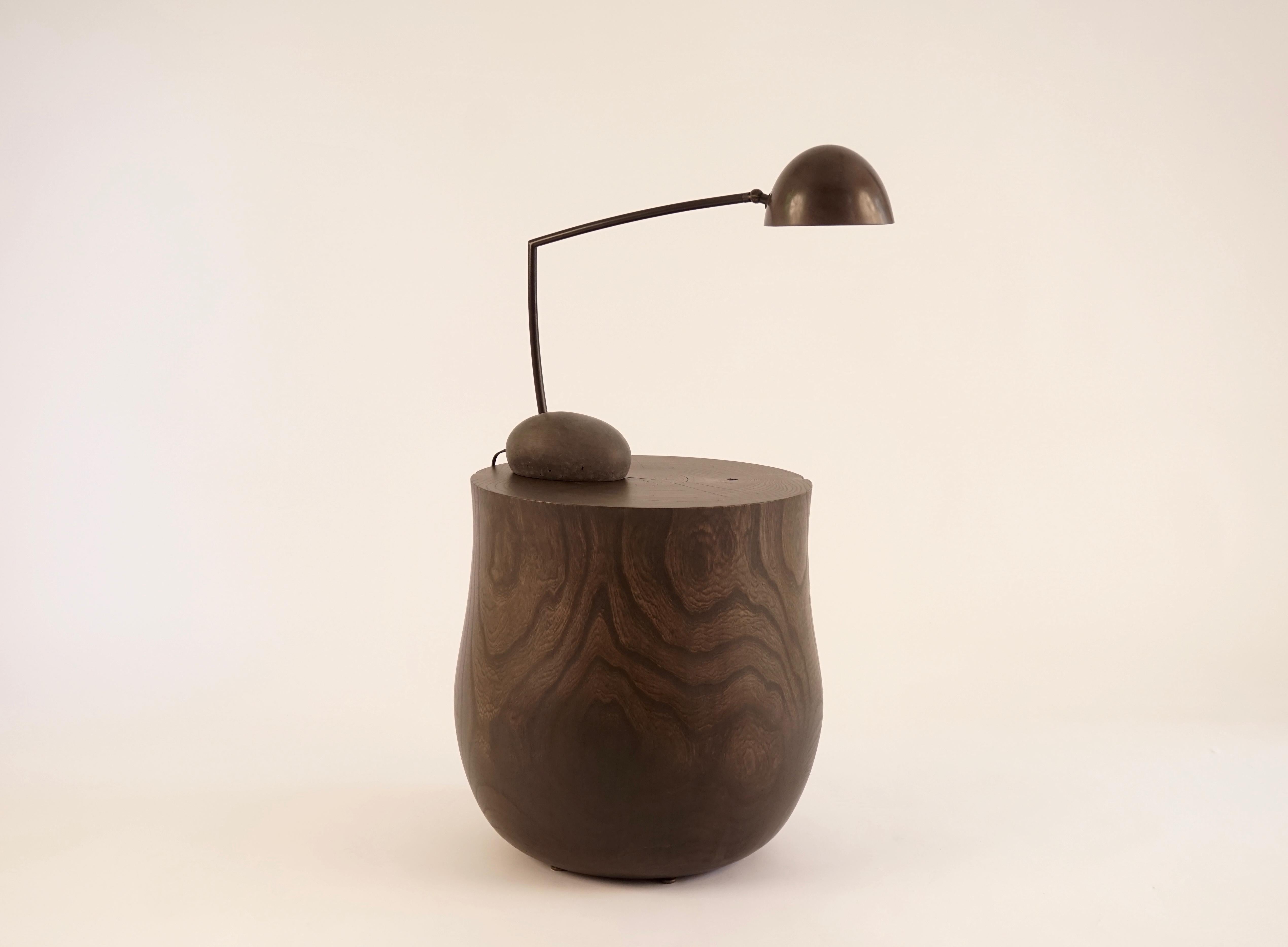 This is the small version of the Skye table lamp. This darkened cement base was made with forms taken from actual stones from the Isle of Skye. The arm and hand spun shade are solid bronze with an acid darkened patina. The shade articulates side to