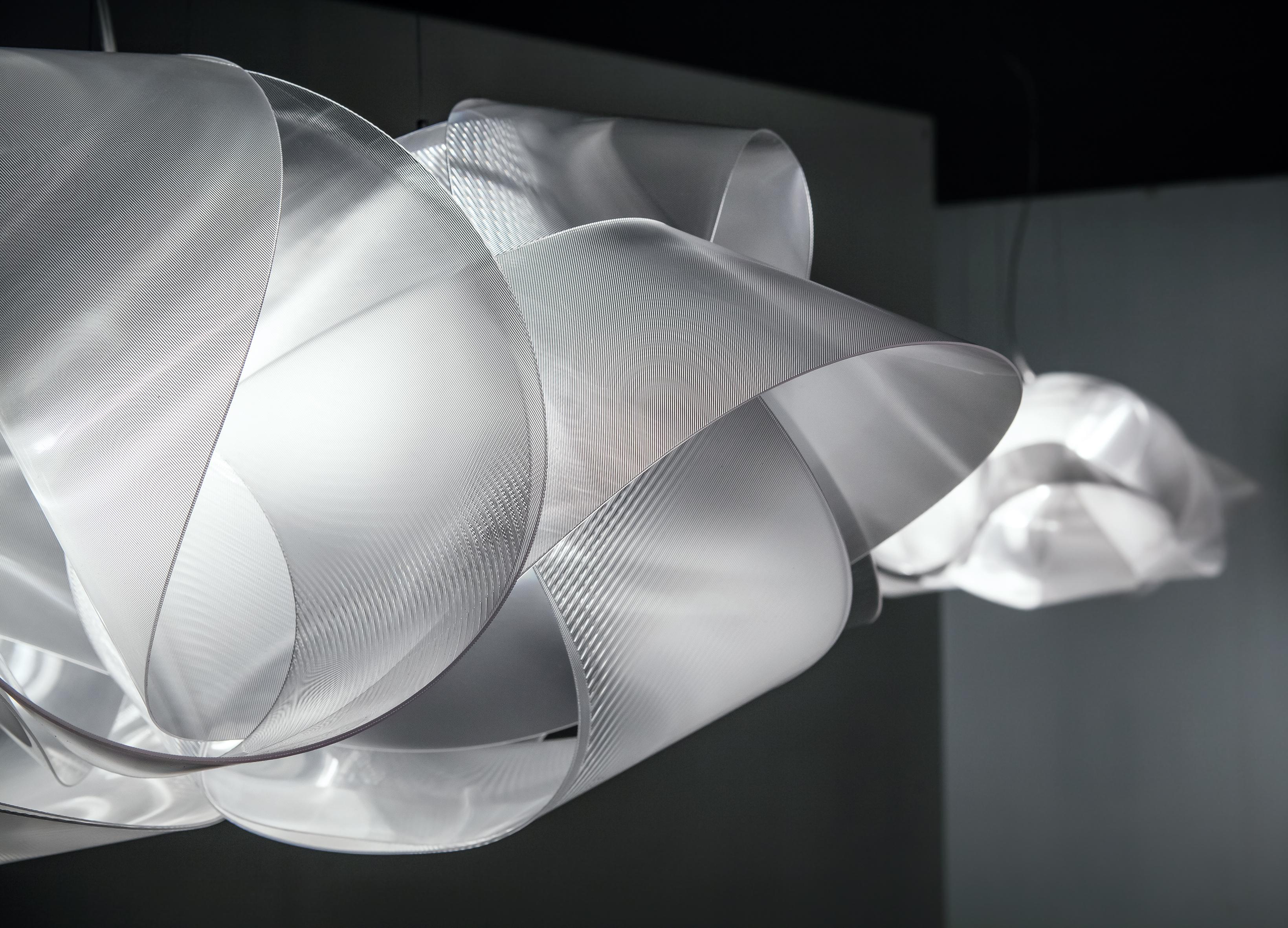 Fabula appears to be a long, silky piece of fabric wound around itself. The new, iridescent versions for ceiling and wall are 60 cm in diameter, handmade with Lentiflex®, and feature 5 light sources that make it perfect for illuminating large