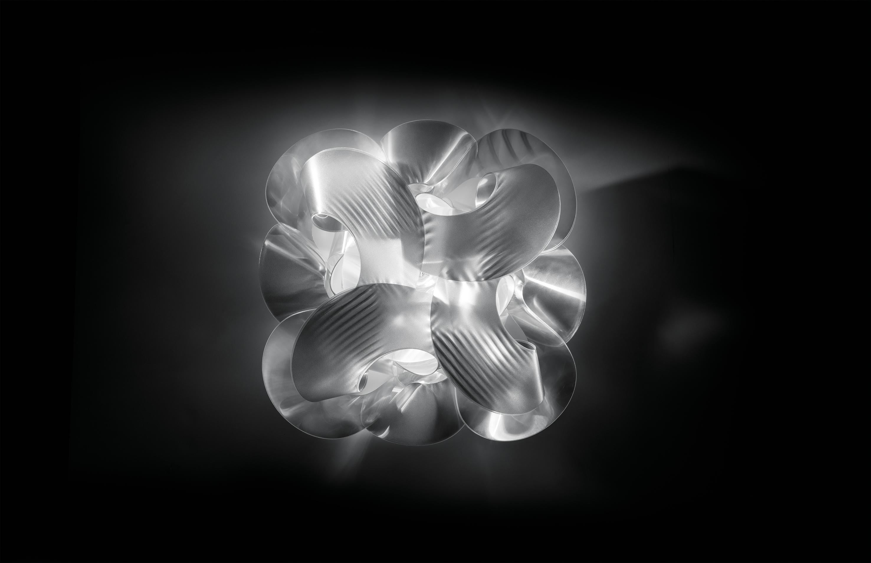 Fabrice semble être un long morceau de tissu soyeux enroulé sur lui-même. Les nouvelles versions irisées pour le plafond et le mur ont un diamètre de 60 cm, sont fabriquées à la main avec Lentiflex® et disposent de 5 sources lumineuses qui les