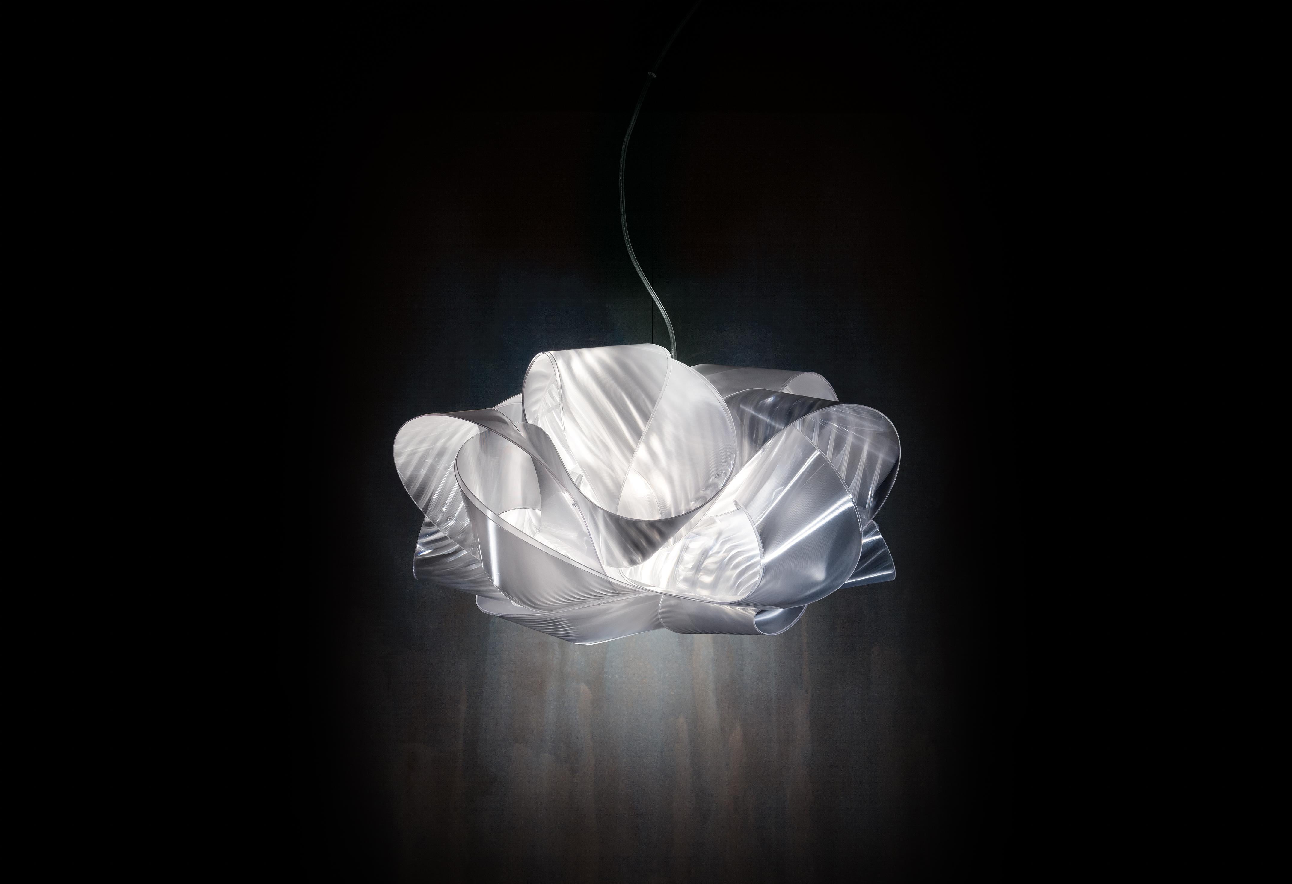 Fabula appears to be a long, silky piece of fabric wound around itself. The new, iridescent versions for ceiling and wall are 60 cm in diameter, handmade with Lentiflex®, and feature 5 light sources that make it perfect for illuminating large