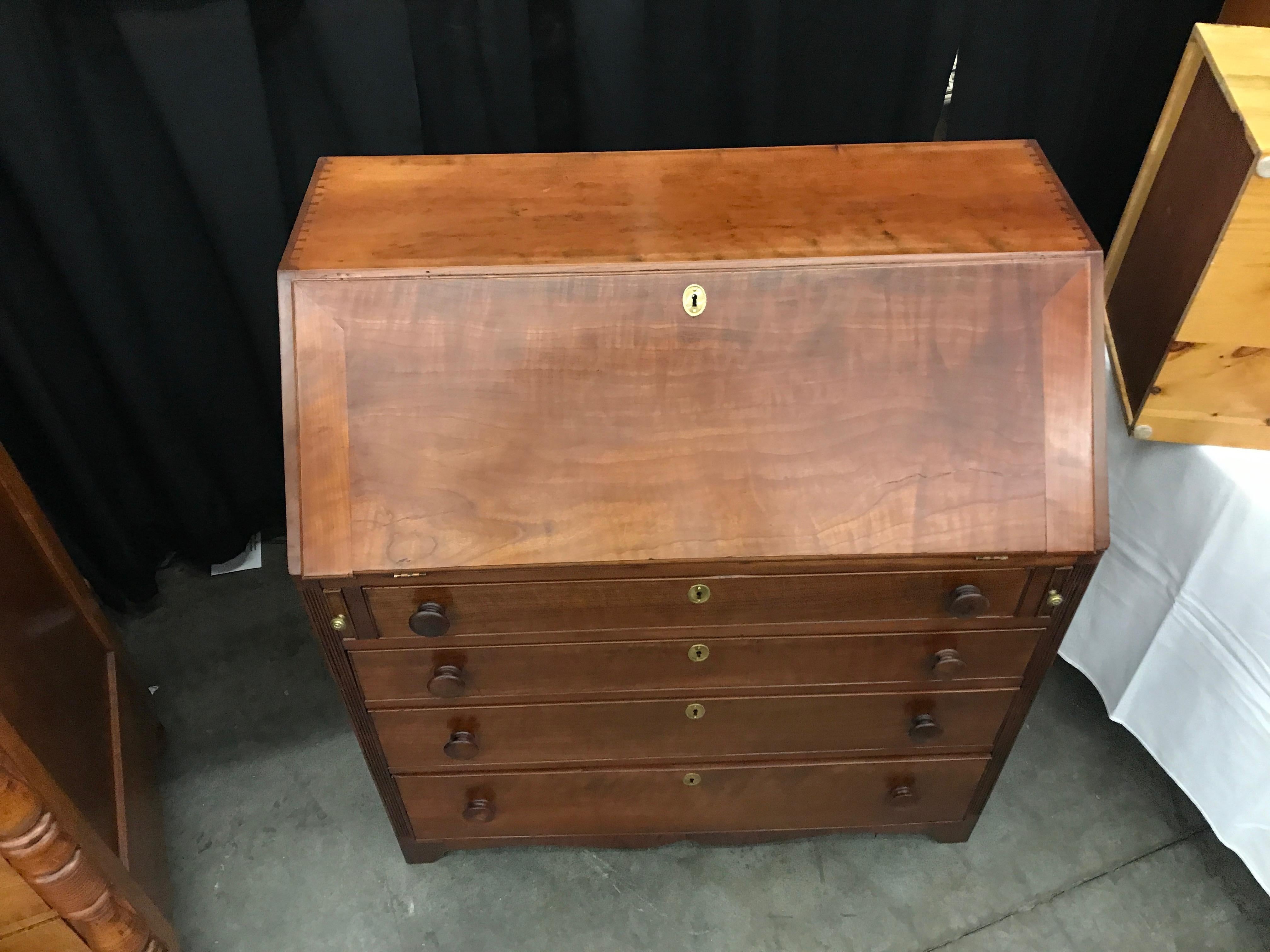 Slant front desk circa 1890 in Figured cherry with wooden knob pulls, brass escutcheons, dovetailed top, reeded borders and graduated drawers. Interior drawers are beautiful and function as they should. Pulls on the lid supports have lion heads on