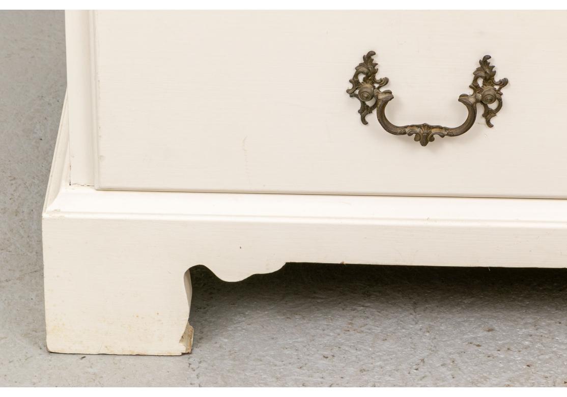 The chest in white paint with two short over two long drawers with baroque style bales and escutcheons (lacking a key). The slant front opens to an emerald green painted interior with compartments and cubby holes. Raised on a carved skirt with