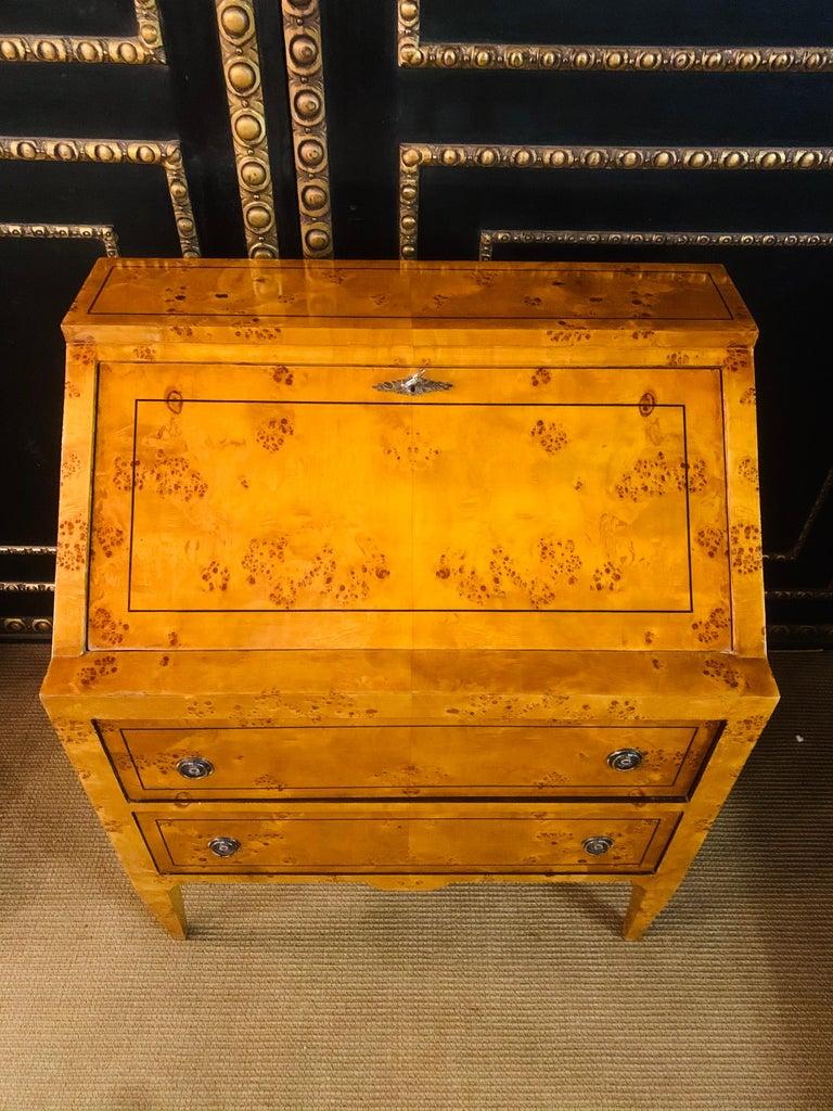 Exotic maple root veneer on solid softwood. Straight, two-drawer body above short, conical square legs, above an inclined writing flap and staggered office division of drawers and compartments. Classicist fittings with hand rims.

Nice patina,