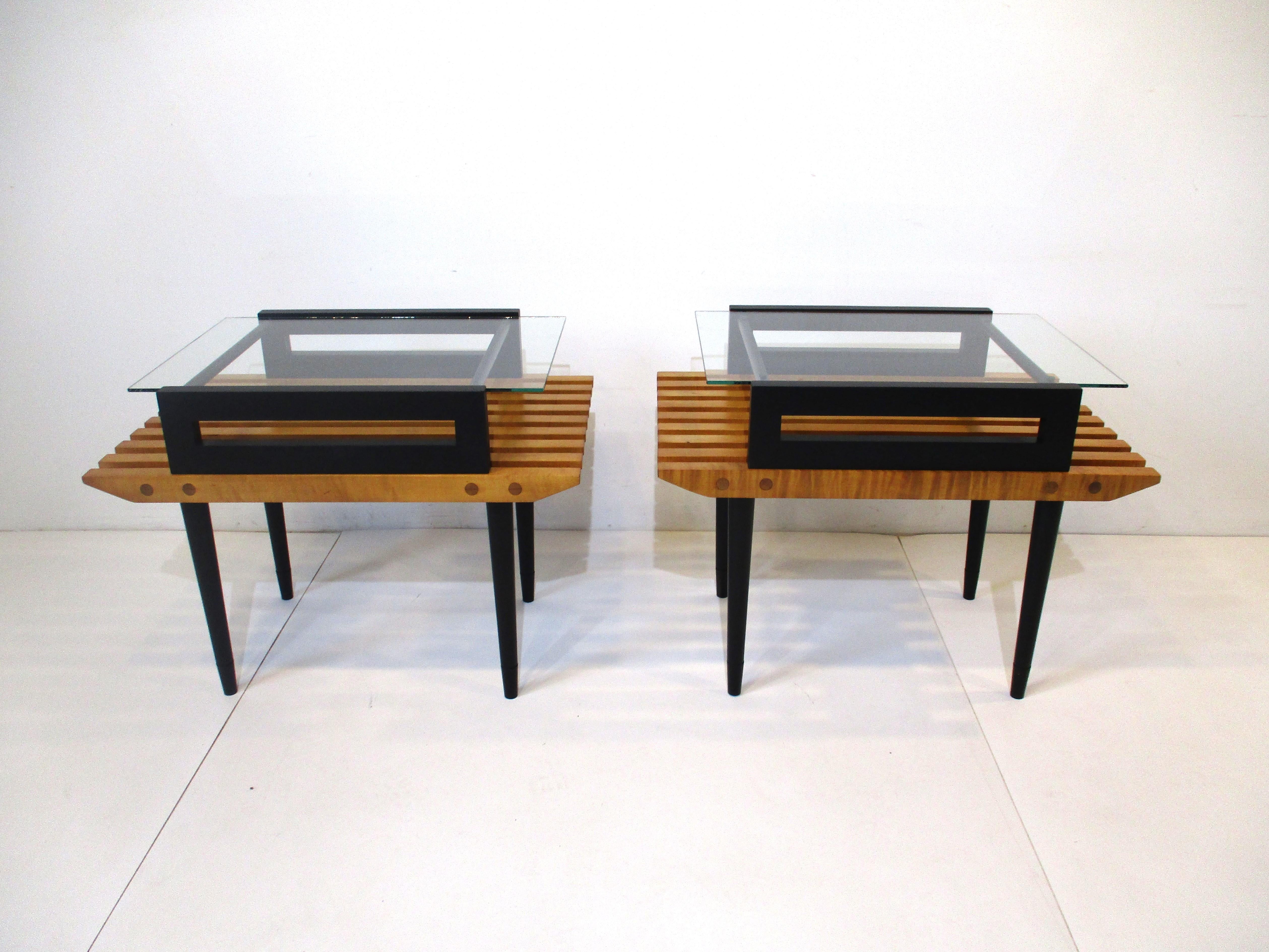 A pair of heavy well crafted solid maple slat wood side / end tables with satin black legs and upper shelve . A glass insert to the top gives the pieces a light clean look having beveled front and rear slats and dowel construction show the quality
