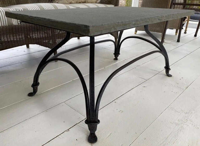 Indoor or outdoor French bistro style metal base garden coffee or cocktail table with slate top married to a bronze colored wrought iron base that is secured by gracefully arched stretchers and ended at the bottom by padded feet. Top and base can be