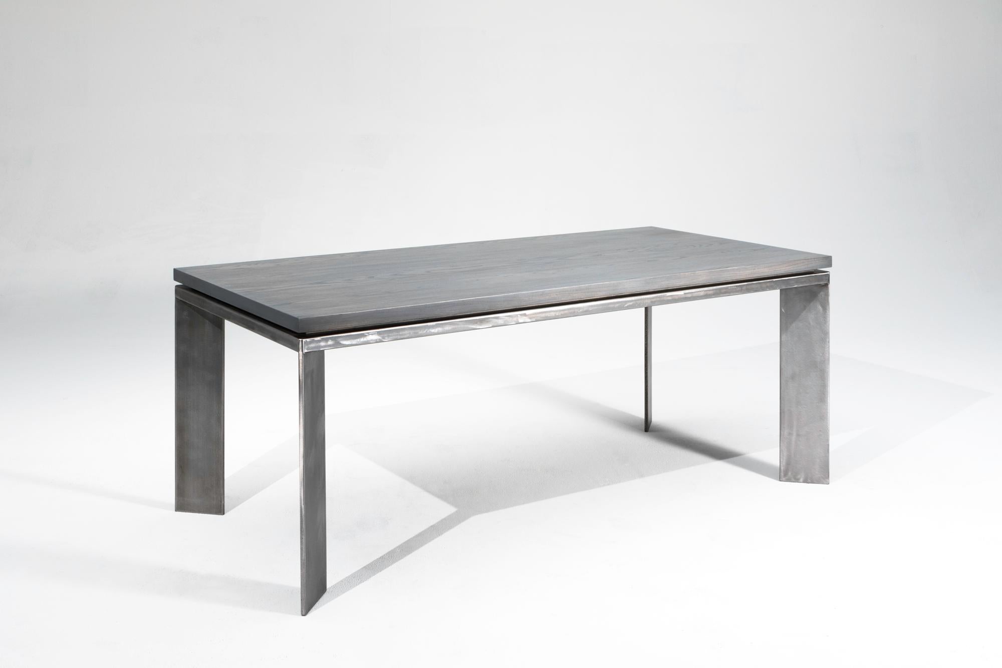 Der Charlevoix hat ein sehr klares und einfaches Design. Die Tischplatte aus massivem Eschenholz ist in Schiefergrau gehalten und wird von einem Sockel aus gebürstetem Stahl begleitet. Die massive Platte ist leicht über den Sockel angehoben, um