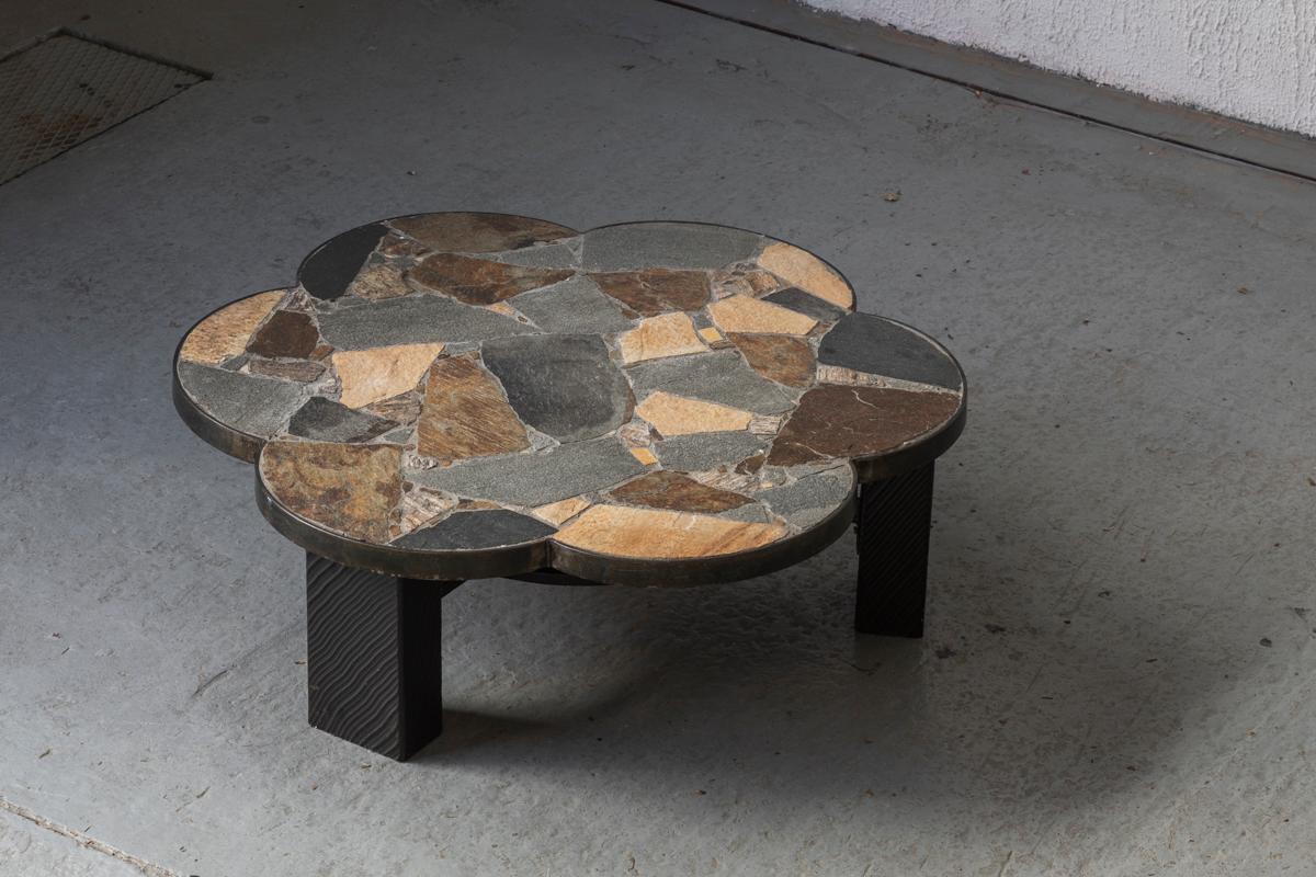 Brutalist slate stone coffee table, designed and produced around 1950. The table top is flower-shaped with an inlay of different kinds of stone, giving it a gorgeous terrazzo look. The table top is supported by three black, wooden blocks with a