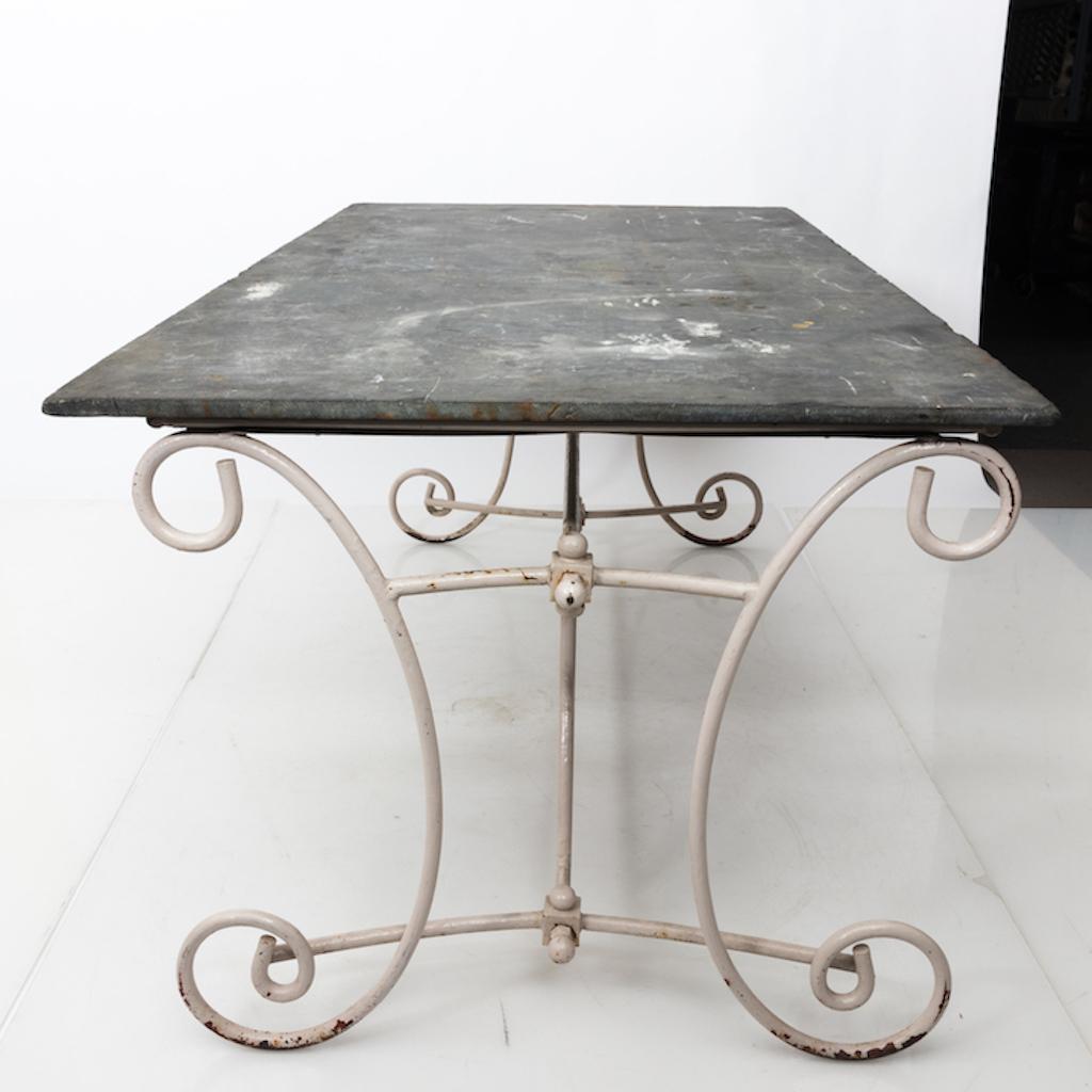 Lovely outdoor dining table with sculptural iron scroll base from England. Nice weathered surface to the original slate gray top. A romantic addition to an English Country style garden or conservatory.

