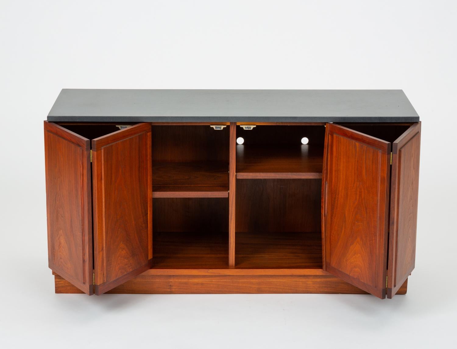 A walnut case piece from North Carolina-based Founders Furniture designed in the 1950s by Jack Cartwright. This small sideboard, known as the Half Cabinet, features beautifully figured walnut wood and slate top. Four panels make up two folding