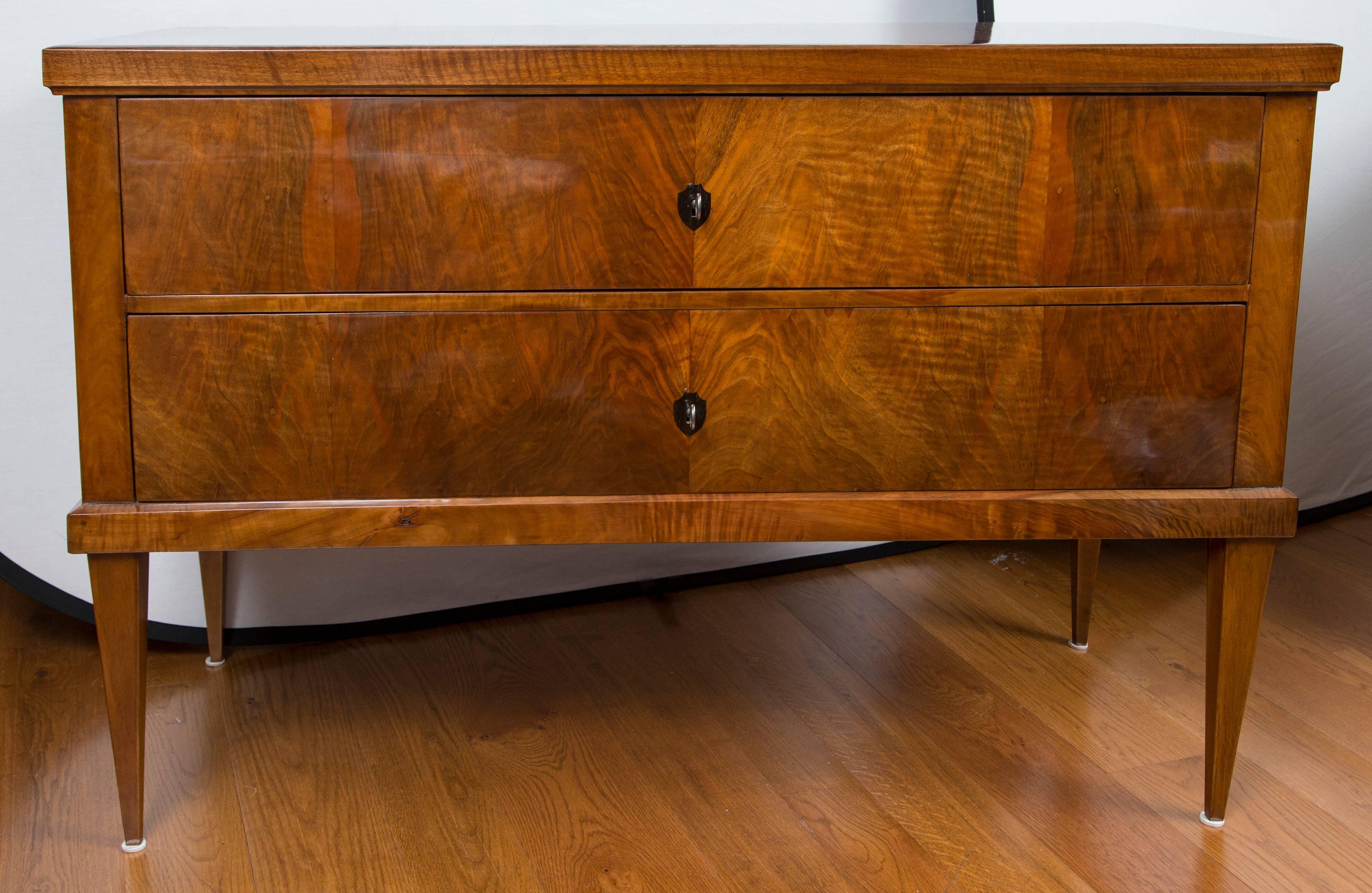Large Biedermeier chest in a darker walnut veneer on pine, comprised of two long drawers on high straight and tapered legs, adorned with inlaid shield-shaped escutcheons.
Date: circa 1840.
Origin: Germany
Condition: Excellent, reconditioned and