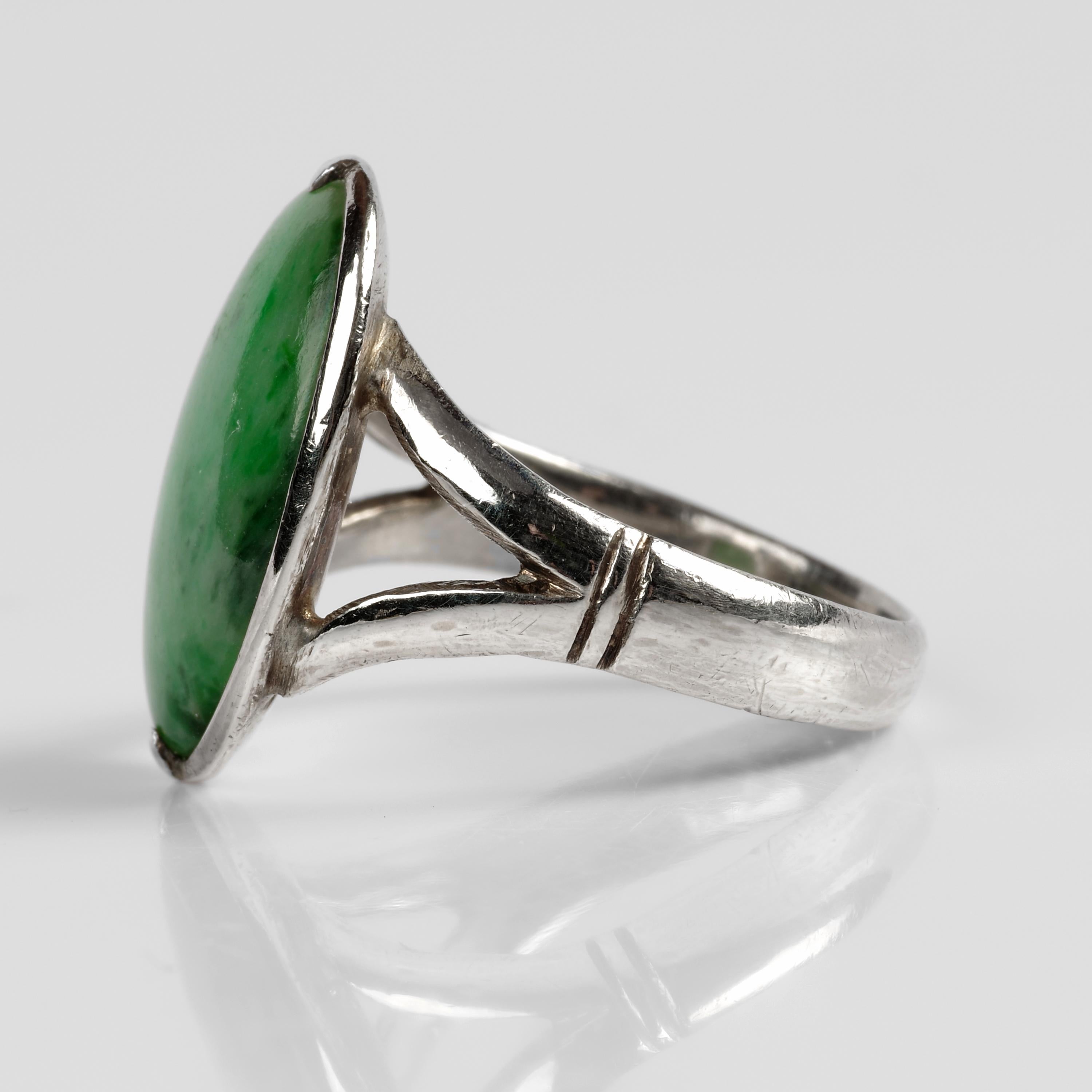 Featuring a large (18.3 x 12.3) oval cabochon of mottled, translucent green jade set within a brilliantly simple hand-made 14K white gold mounting, this late Art Deco-era (circa 1939) ring is a study of sleek simplicity. The highly polished jade