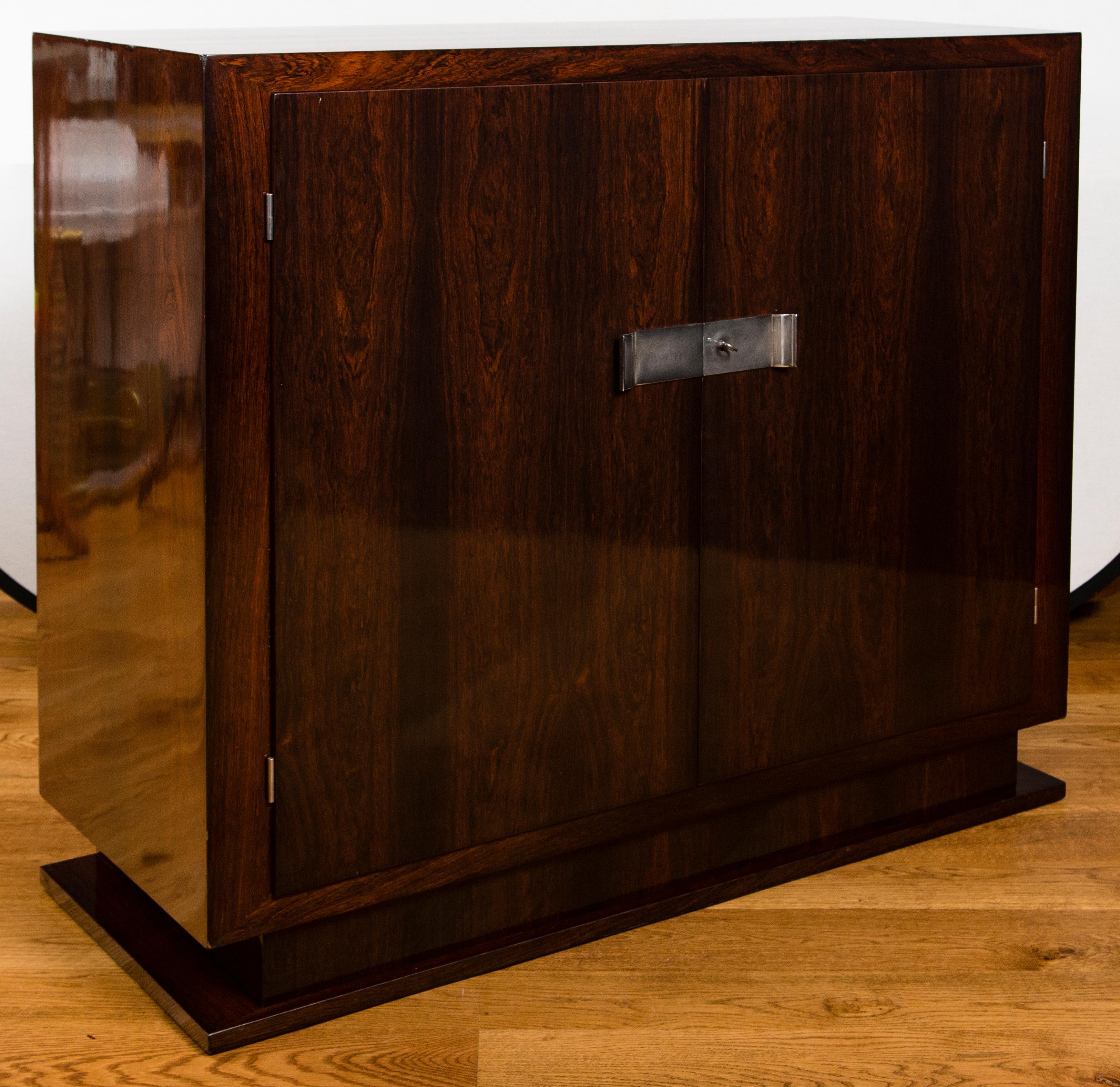A super Art Deco two-door cabinet finishing on a pedestal base shown with nickel plated hardware in beautiful rich stained rosewood veneer.
Sleek two door cabinet/sideboard/bar on a pedestal base in a rich shellaced rosewood adorned with nickel