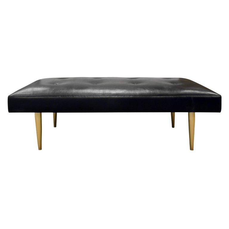 Clean lined bench designed by Milo Baughman for Thayer Coggin. Newly upholstered black leather seat; tufting and piping add visual interest. With conical gold legs. Perfect for extra seating or a bench at the end of the bed.