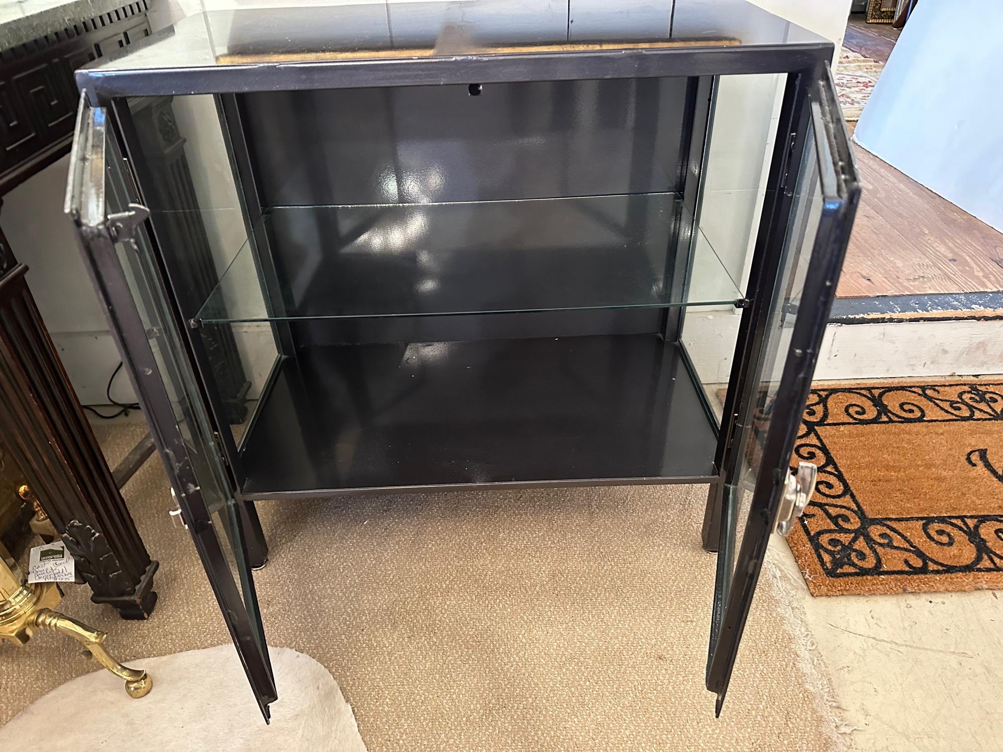 Sleek industrial medium sized blackened dark grey steel and glass cabinet having transparent doors and sides, silver steel hardware and one interior shelf.  Great size for a bathroom.