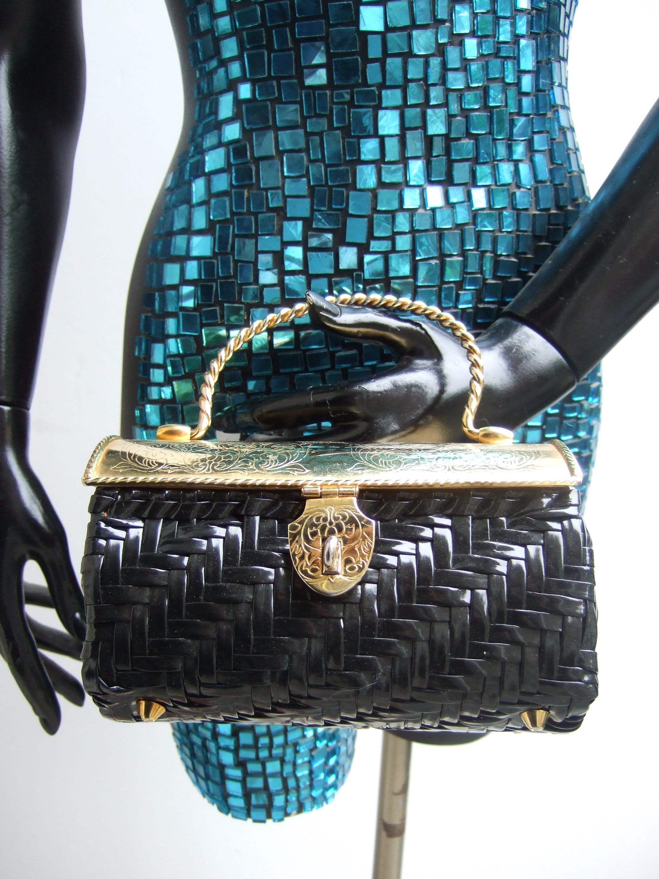 Chic gilt metal black woven vinyl cylinder box purse c 1970s
The stylish retro handbag is designed with a gilt metal curved 
hinged lid cover with subtle impressed scrolled detail

Carried with a braided gilt metal swivel handle. Constructed with