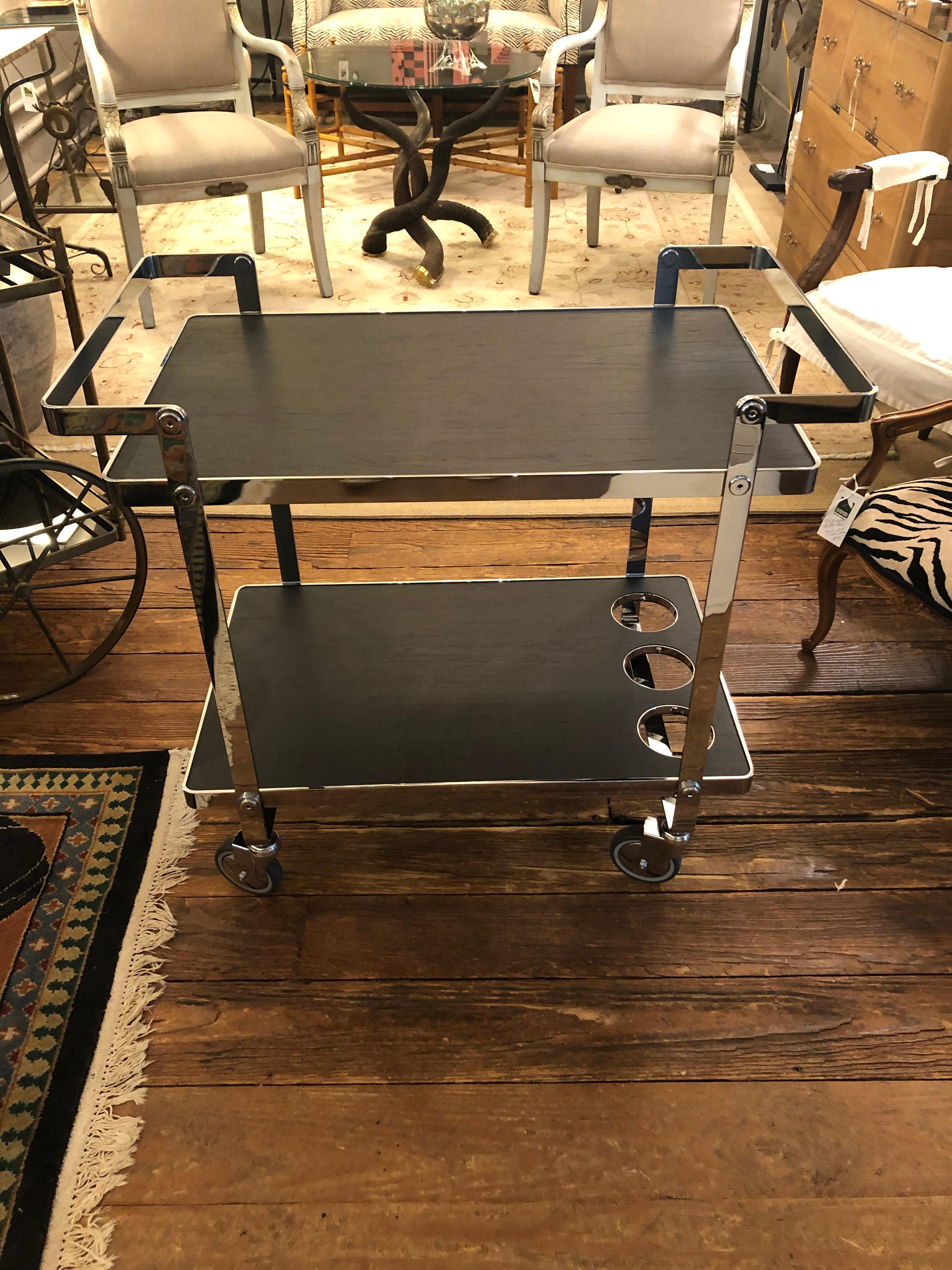 A very glamorous sleek bar cart having a mix of shiny chrome and matte finish black wood laminate. Bottom tier has holes for bottles. Wheels roll super smoothly and are marked Made in Italy.
Measures: 28.5 W top tier
26.75 H top tier
2nd tier 9.5