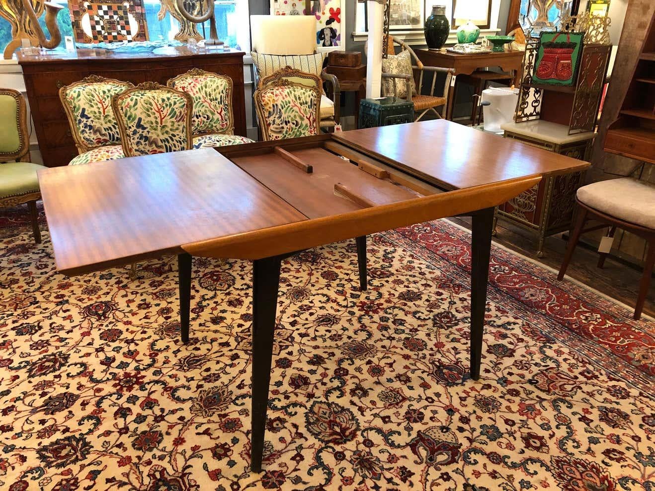 Early original sleek & clever English G Plan Mid-Century Modern dining table having ingenious design with hidden single leaf that spins over to extend the table to 59.5. Legs are tapered, elegant and ebonized to make a nice contrast with the rich