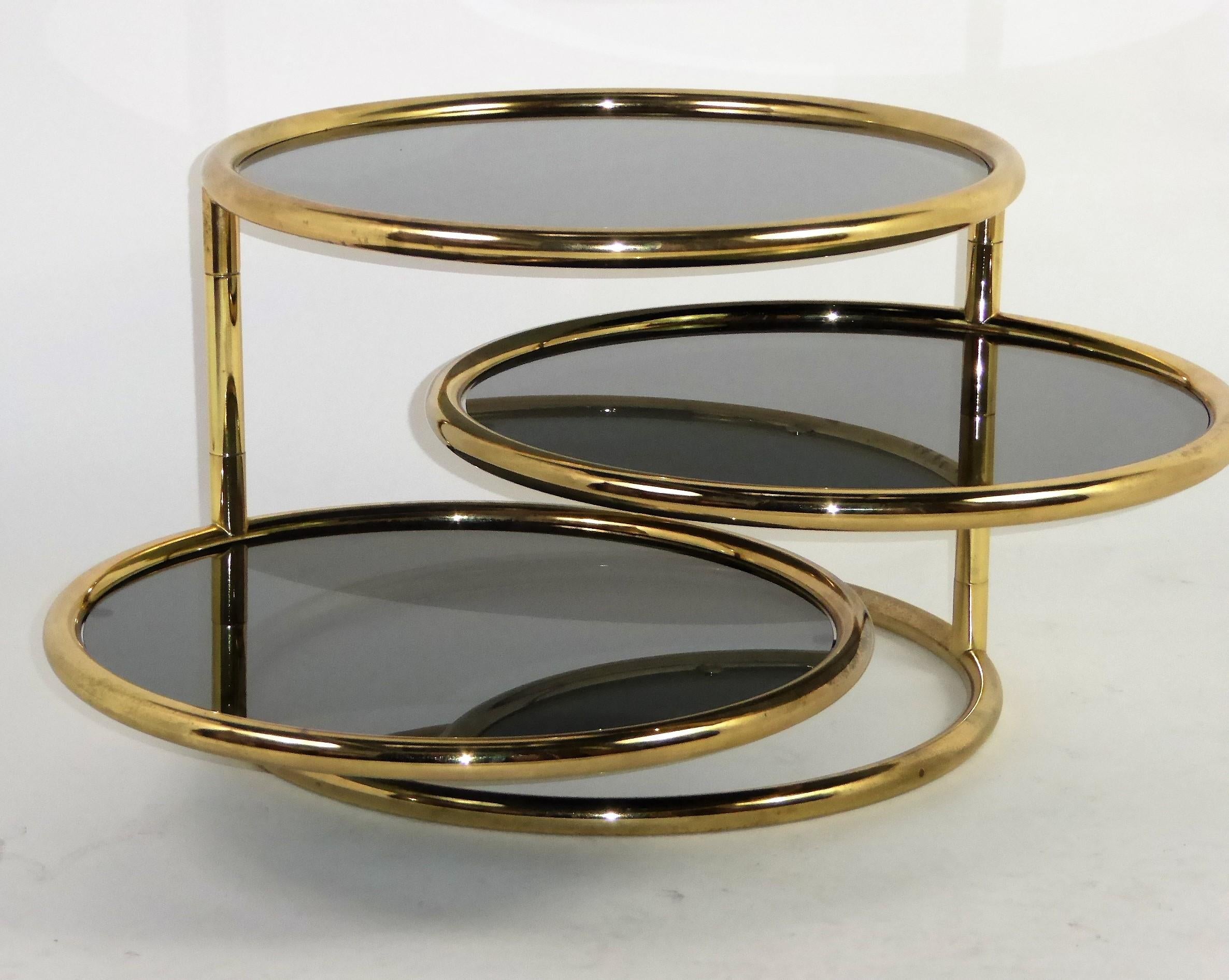 1970s Milo Baughman attributed Tubular brass and dark Smoked Glass Swiveling Coffee Table. A Cocktail Table that transforms itself by swiveling out the two movable tiers to any angle desired. The brass with an age darkening that adds to its