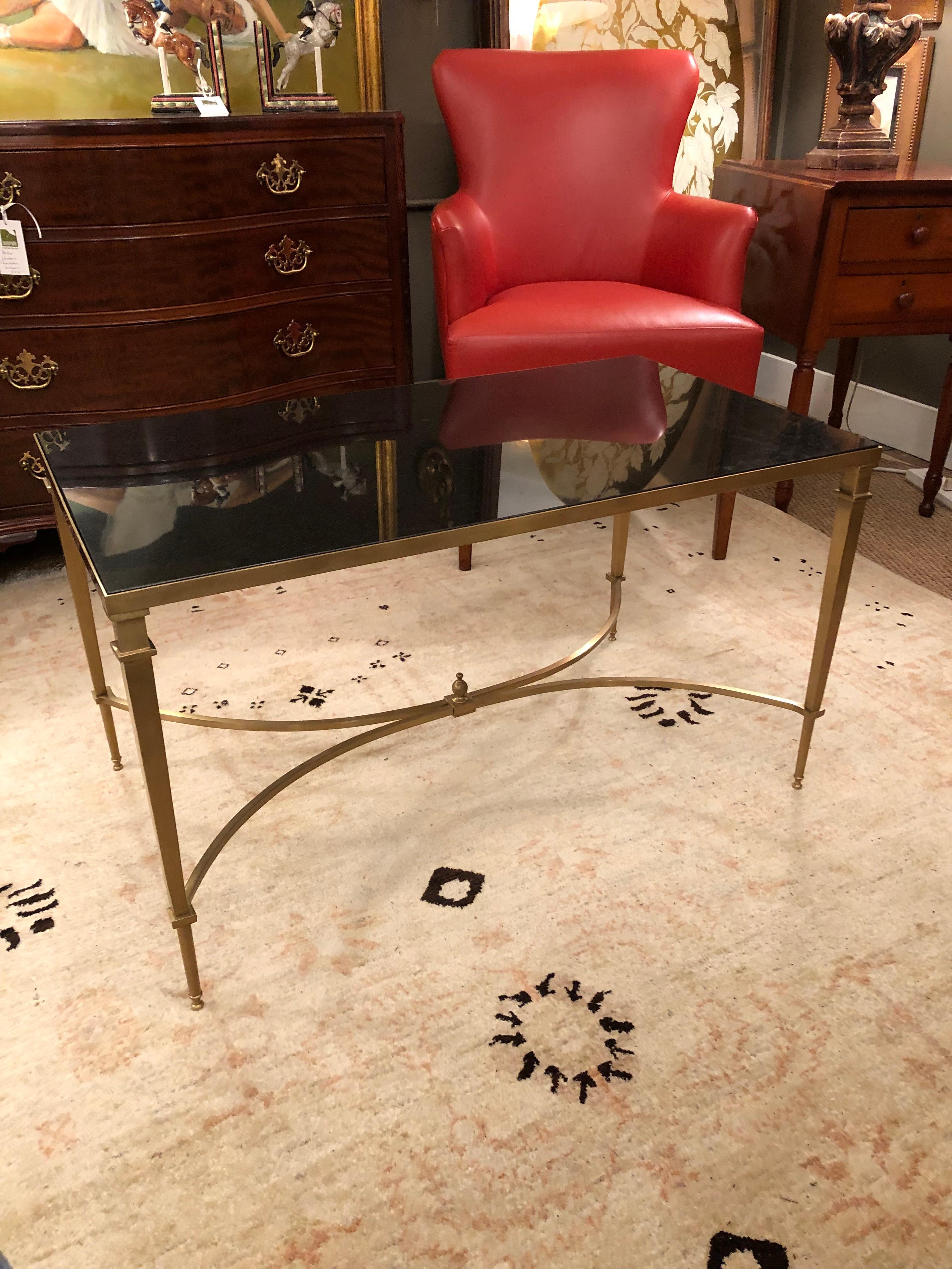 A sleek elegant rectangular coffee table having striking warm rubbed bronze finish brass offset by black granite top. The elegant legs and stretcher with finial are thin, but heavy and beautifully made.