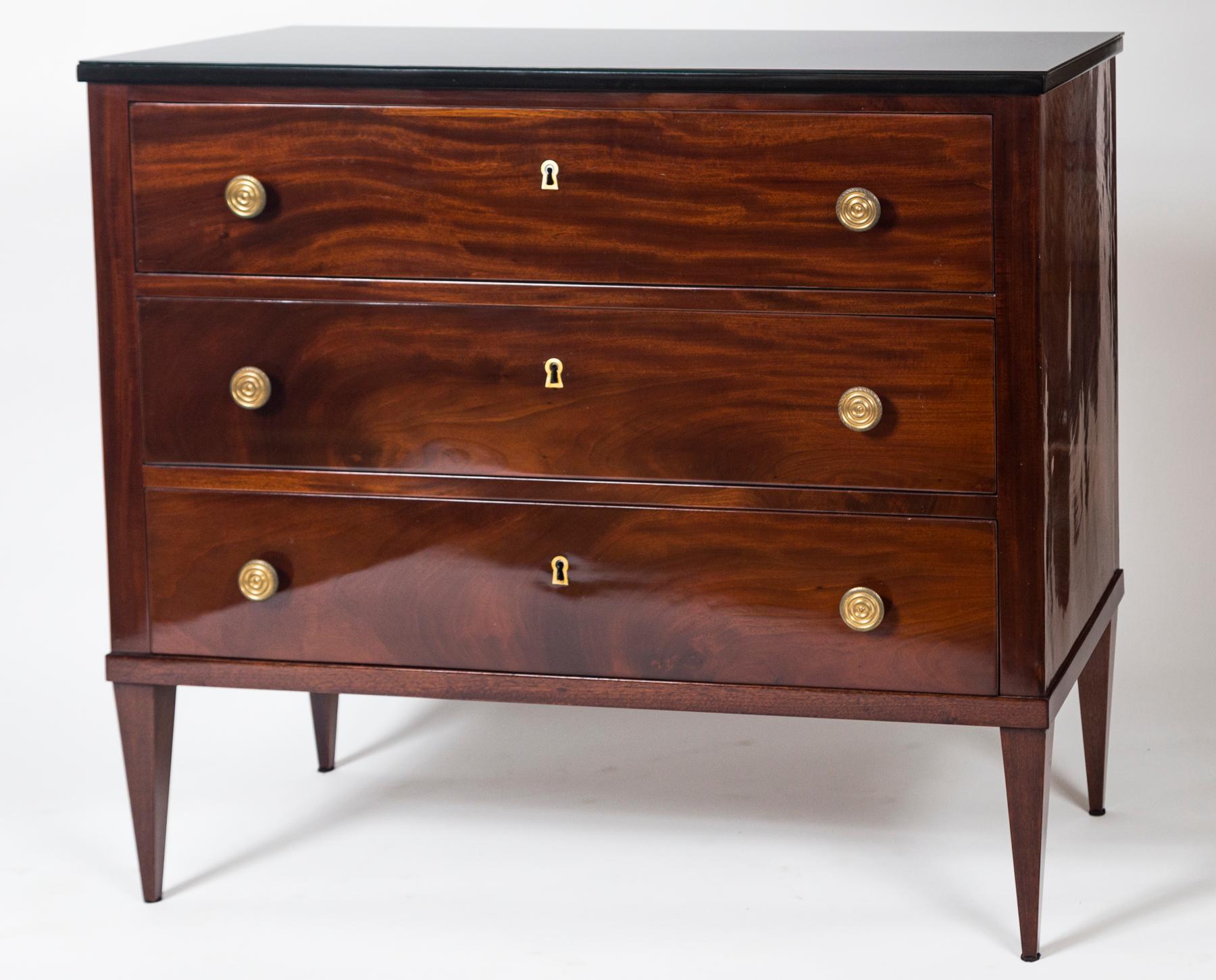 A fine pair of mahogany veneer chest comprised of three drawers finishing on high straight tapered legs and adorned with bronze pulls. Shown with a refurbished black glass top creating an elegant and modernized feel.

Dating: 1825ca

Origin: Berlin,