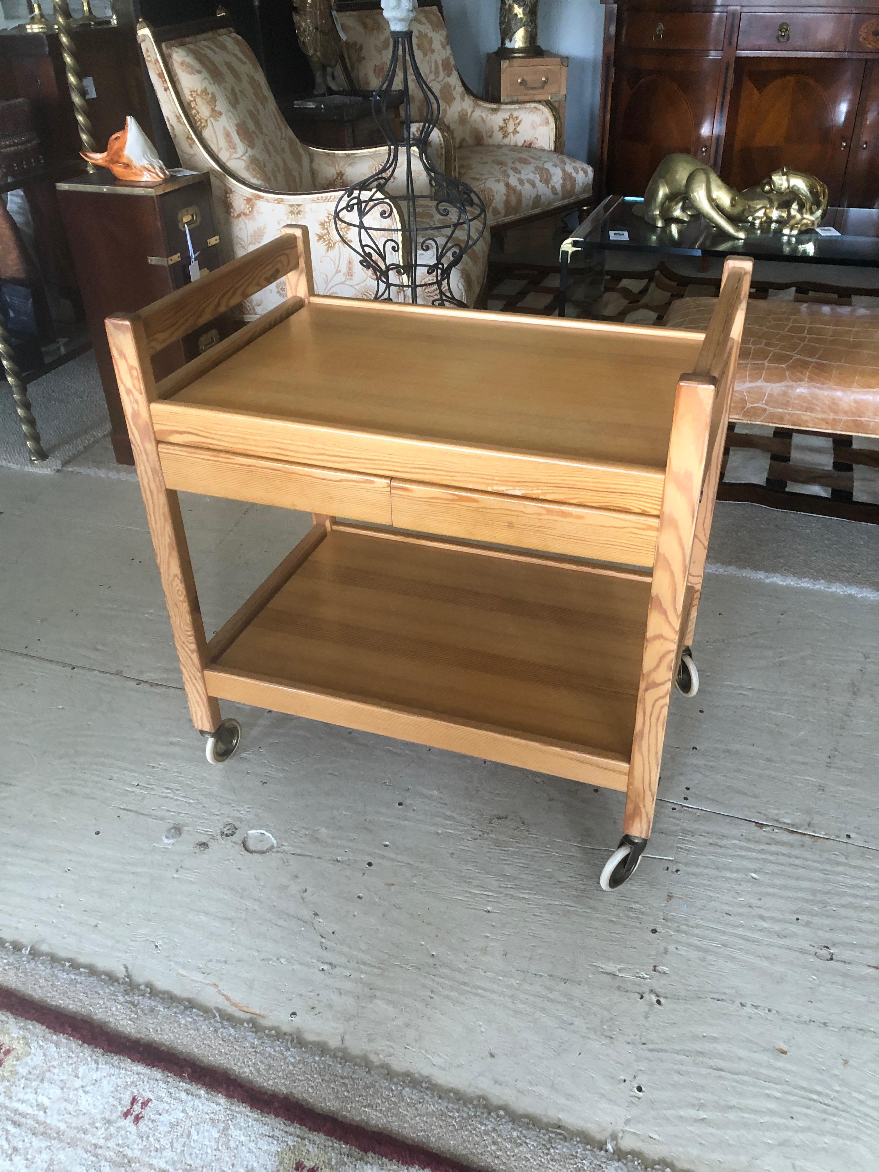 Sleek Mid-Century Modern Danish bar cart constructed o handsomely grained teak with two tiers and two handy drawers under the top service. Original vintage casters that function smoothly. Measures: To top tier 25 H; to bottom tier 8.5 H.
