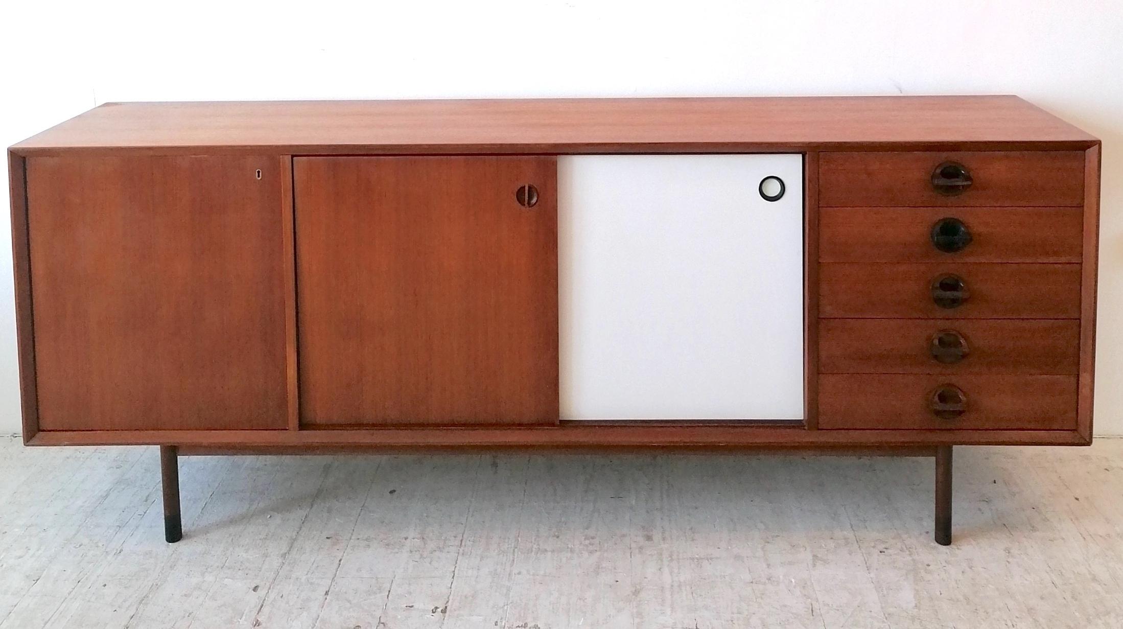 A sleek mid century 1960s Italian 'Monika' sideboard by Faram. Teak veneer with two reversible sliding doors. Indented door pulls. Drawer pulls are sculpted solid wood. The reverse side of the sliding doors is white laminate with inset ebonised wood