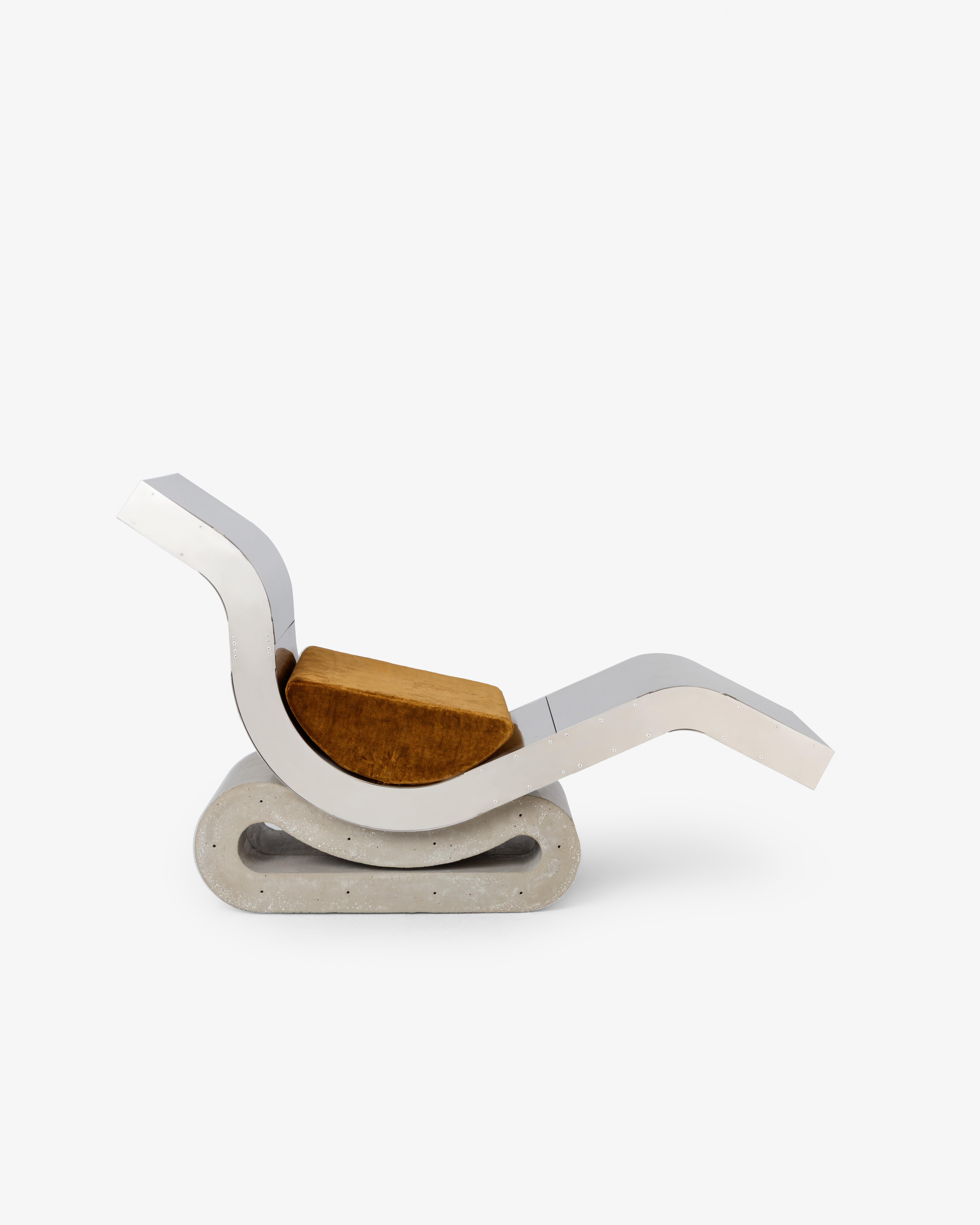 Esta chaise longue de la colección Colendra de Simões equilibra la precisión arquitectónica con la audacia escultórica. Un cuerpo sinuoso de acero inoxidable descansa sobre una base de hormigón, contrastando el peso con la fluidez. Un cojín de