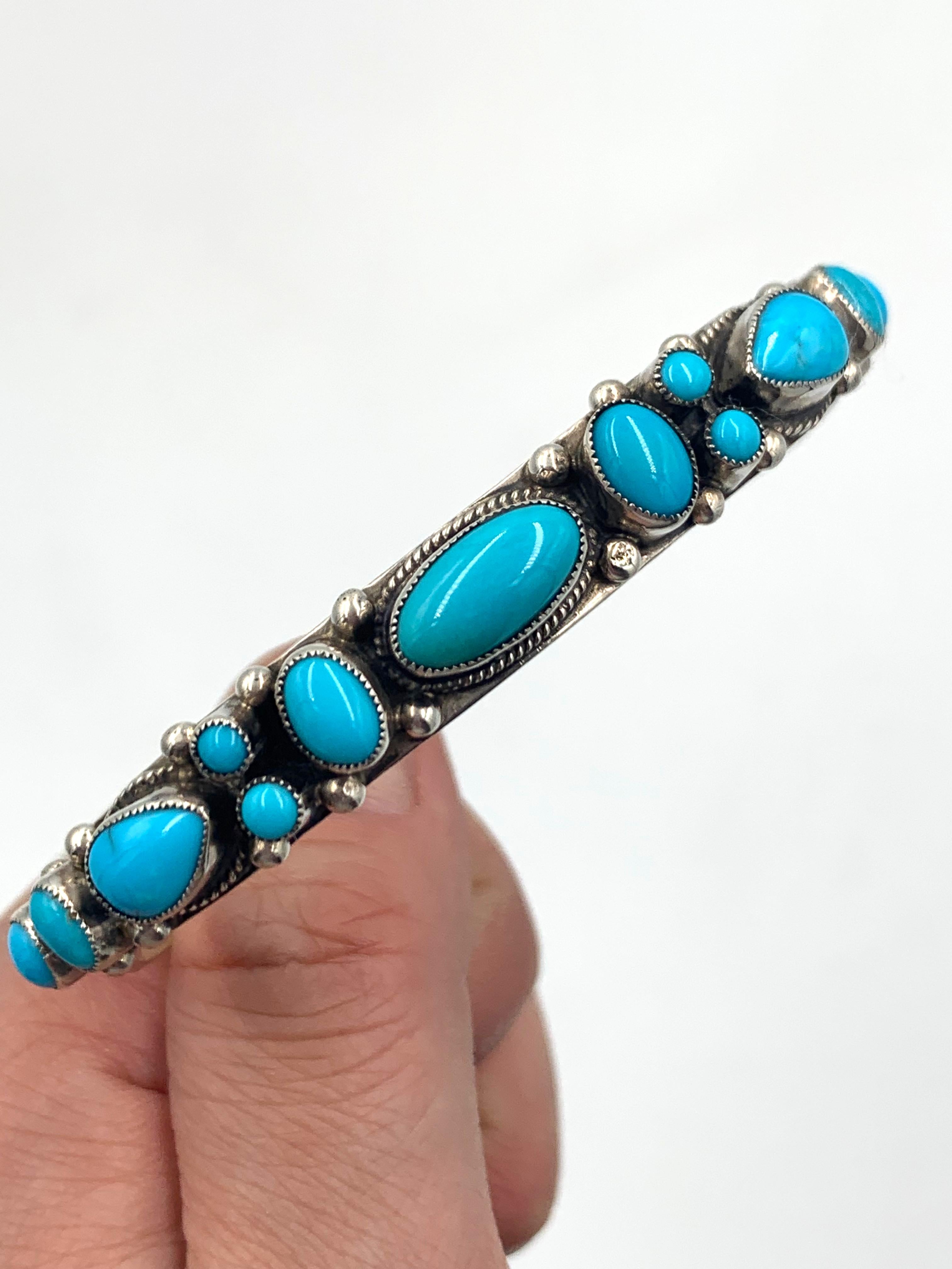 Sterling silver bracelet with 13 sleeping beauty turquoise stones. The 3/8” wide cuff has silver “raindrops” between the stones and hand stamping. Leo Feeney is the silversmith.

Inside measurement: 5 3/8” with a 1” gap

Each Leo Feeney piece is set