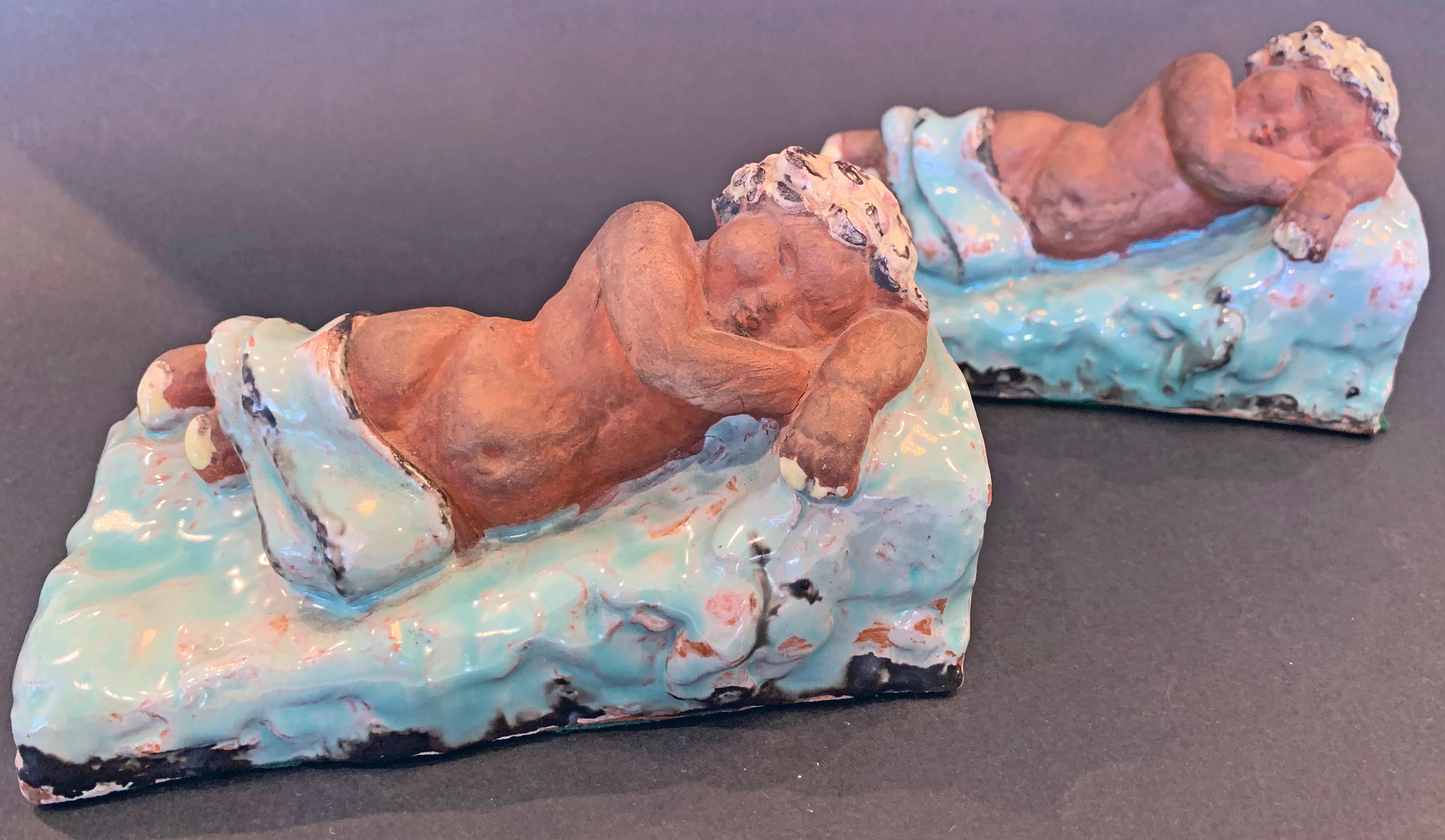 Entirely charming and winsome, this pair of bookends depicting nude children with golden hair who are sleeping on pale blue beds, was probably executed by one of the ceramic artists associated with the Wiener Werkstätte (or Vienna Workshop) in the