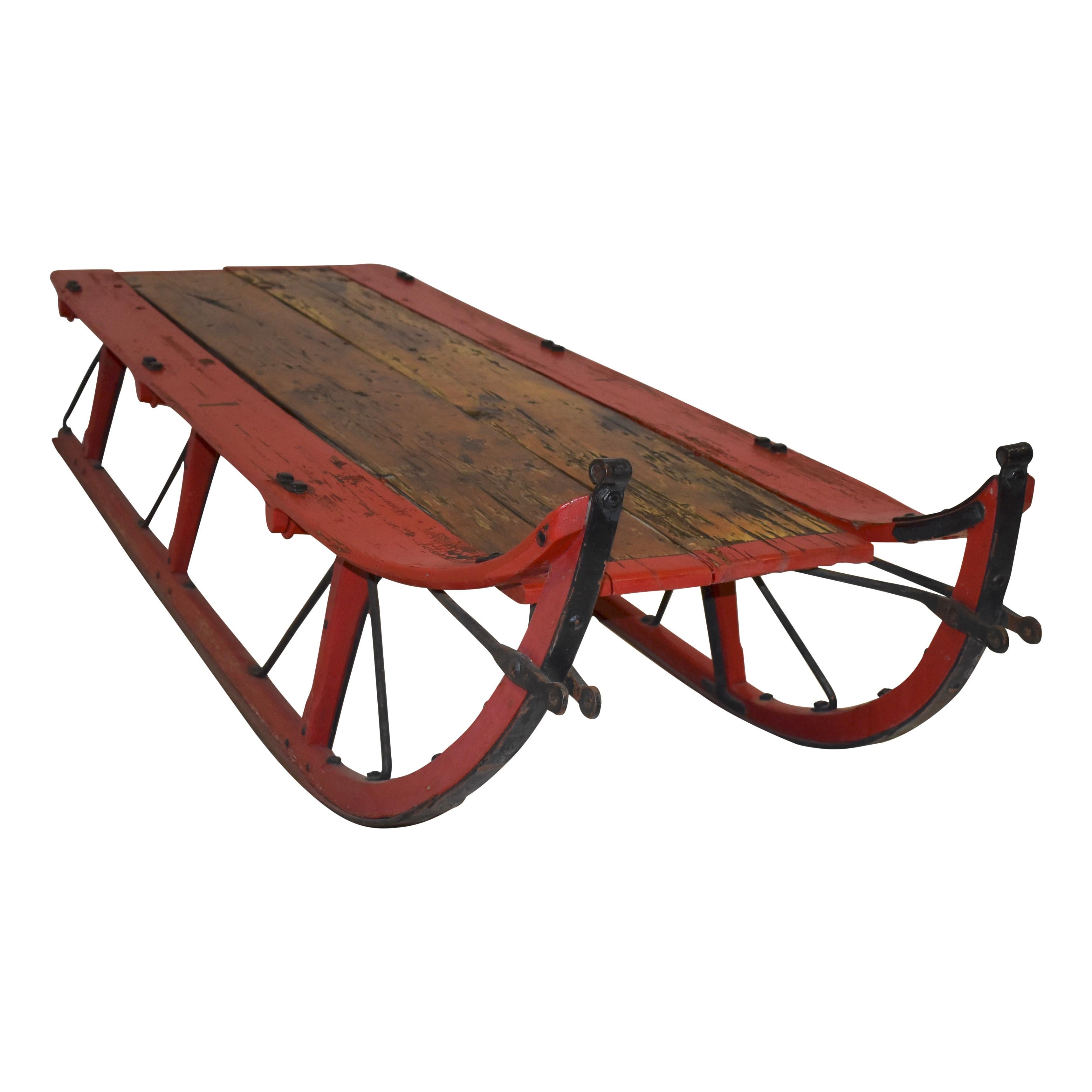 Crafted from antique sleigh runners and reclaimed wood, this rustic coffee table features long, wooden runners with metal runner glides from the turn of the century, giving the table a substantial footprint. Distressed red paint adds to its rustic
