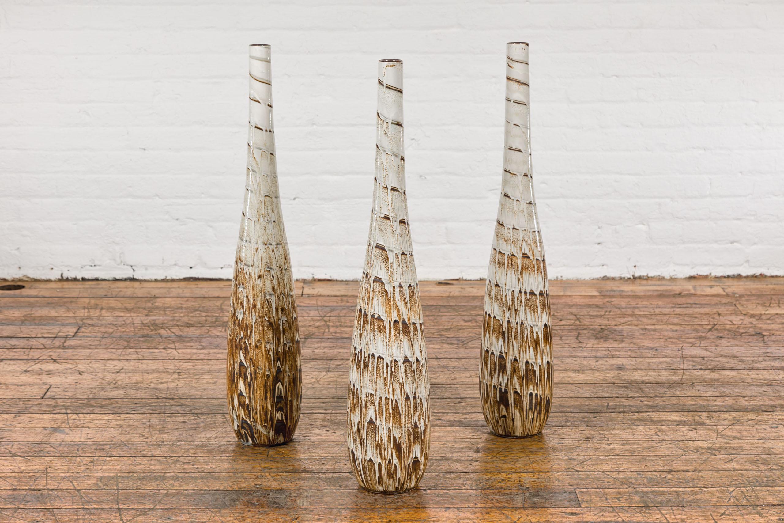 Three slender hand-crafted ceramic vases with spiraling motifs, brown drip glaze and narrow mouth. These contemporary, hand-crafted ceramic vases stand as a testament to modern artistry, each piece uniquely adorned with spiraling motifs and a
