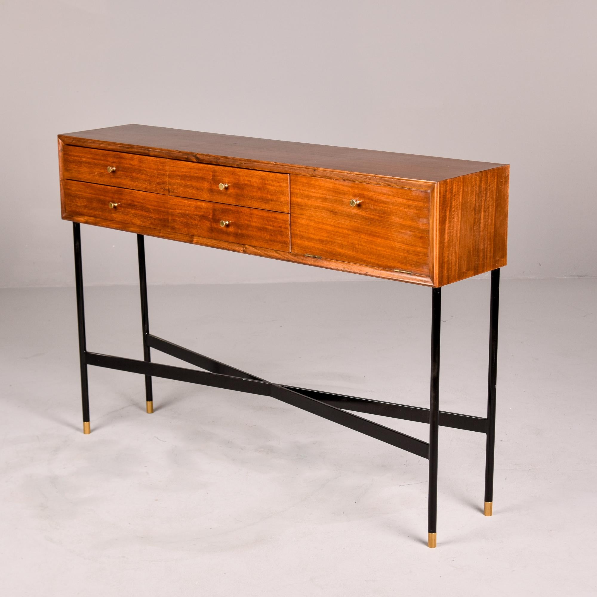 Found in Italy, this slender wood console cabinet on a metal base dates from the early 1960s. The cabinet features four functional drawers with minimalist brass knobs and a storage compartment with drop-down door. Black finished metal base is