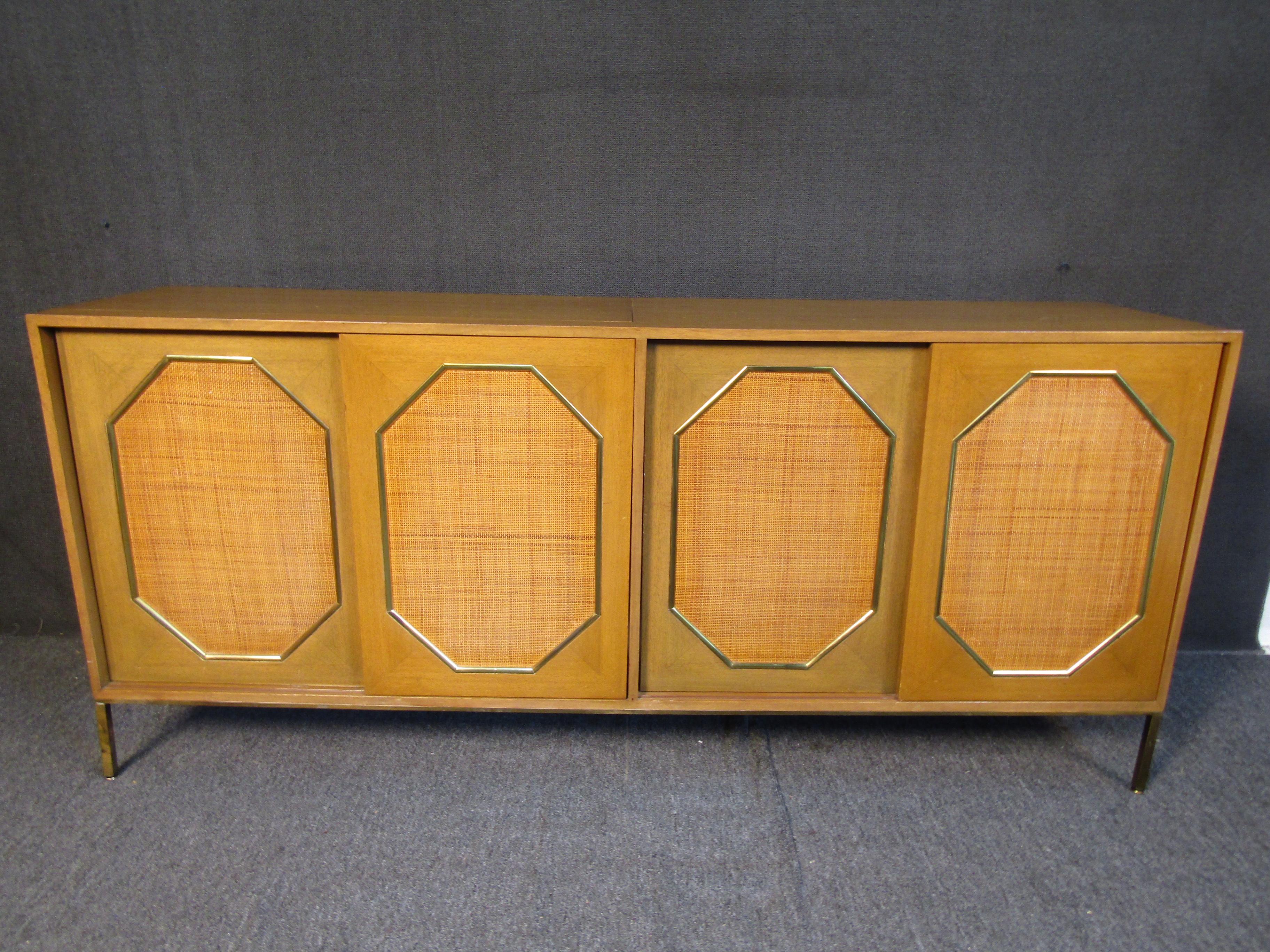 For use as a cabinet or dry bar, this vintage piece by Harvey Probber features a unique design with sliding front doors and an opening top surface. Woven panels on the sliding doors and brass trim make this piece an eye-catching addition to any