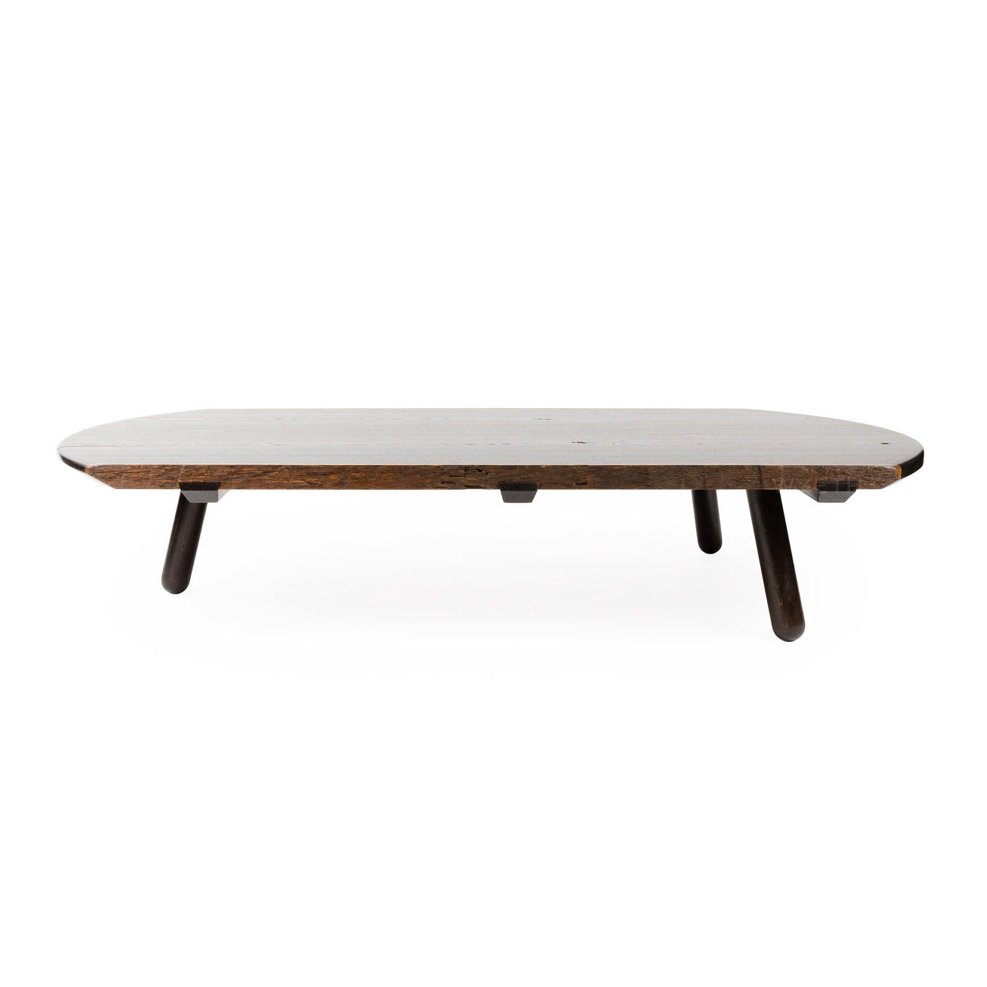 Une table basse faite à la main en chêne fumumé avec une forme ronde, des arêtes naturelles quand elles sont innées dans le bois et trois (3) pieds tournés substantiels qui sont mortaisés à travers le dessus. Le plateau est constitué de chants