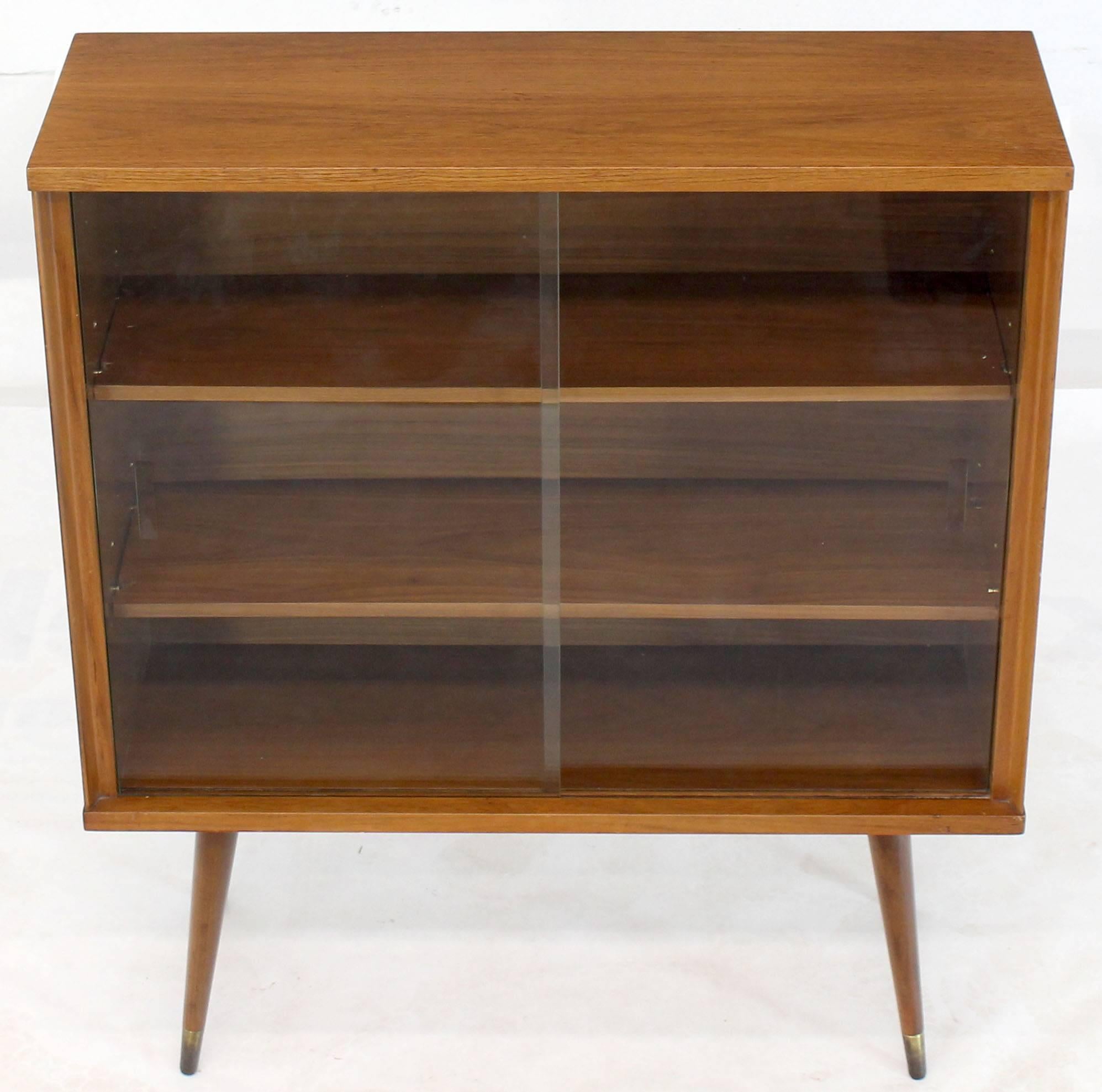 Small Mid-Century Modern bookcase with adjustable shelves and glass sliding doors floating on dowel legs.